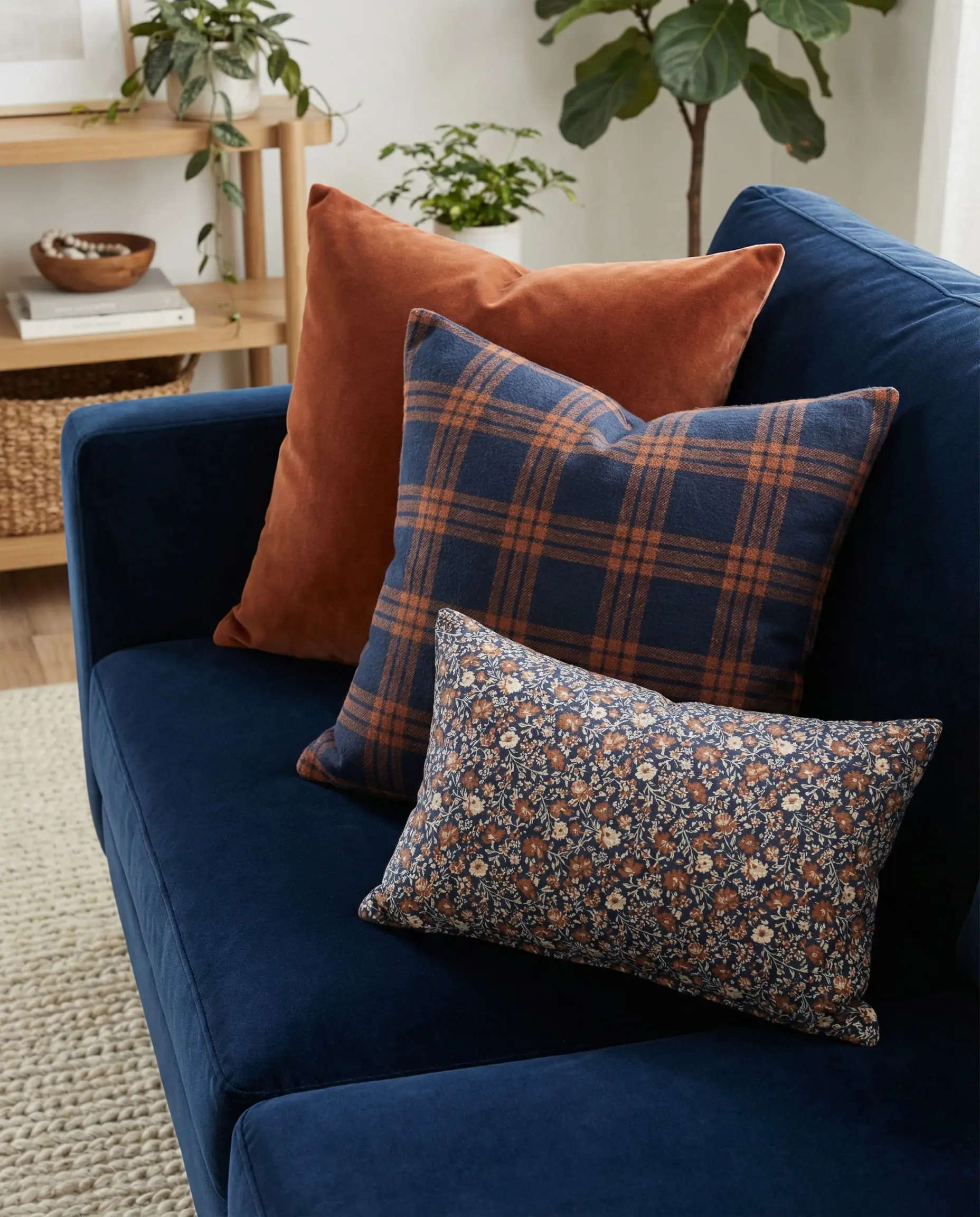 Navy blue couch styled with the rule of three: solid rust, plaid rust/navy, and small floral print pillows.