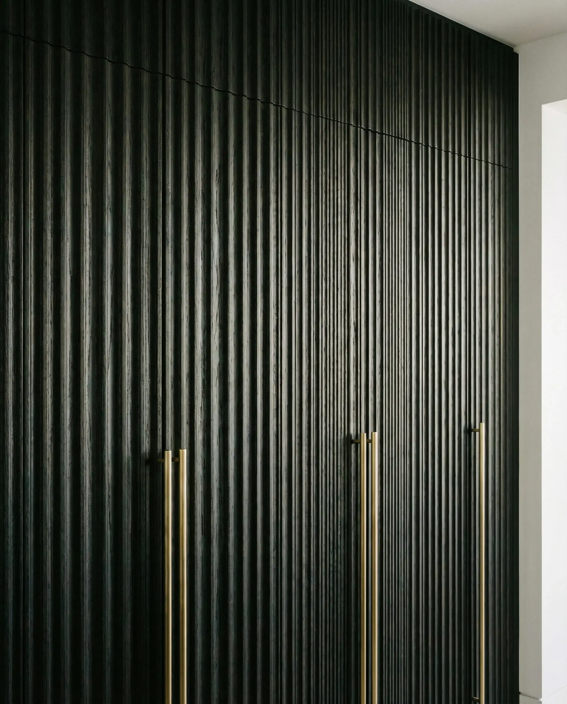 Floor-to-ceiling black stained oak pantry cabinets featuring vertical reeded texture and long brass handles.