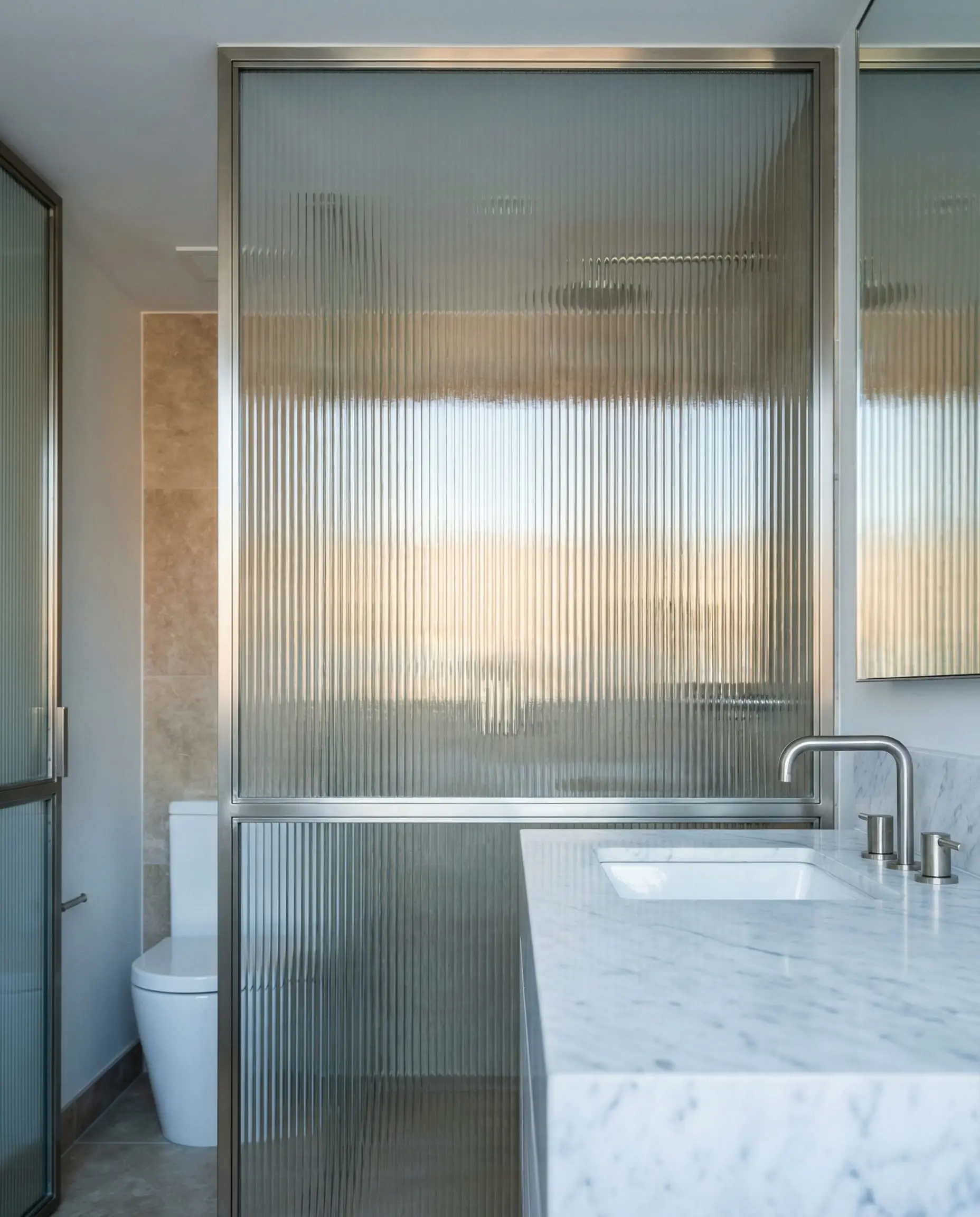 Contemporary bathroom featuring a floor-to-ceiling reeded glass partition wall separating the vanity and shower.