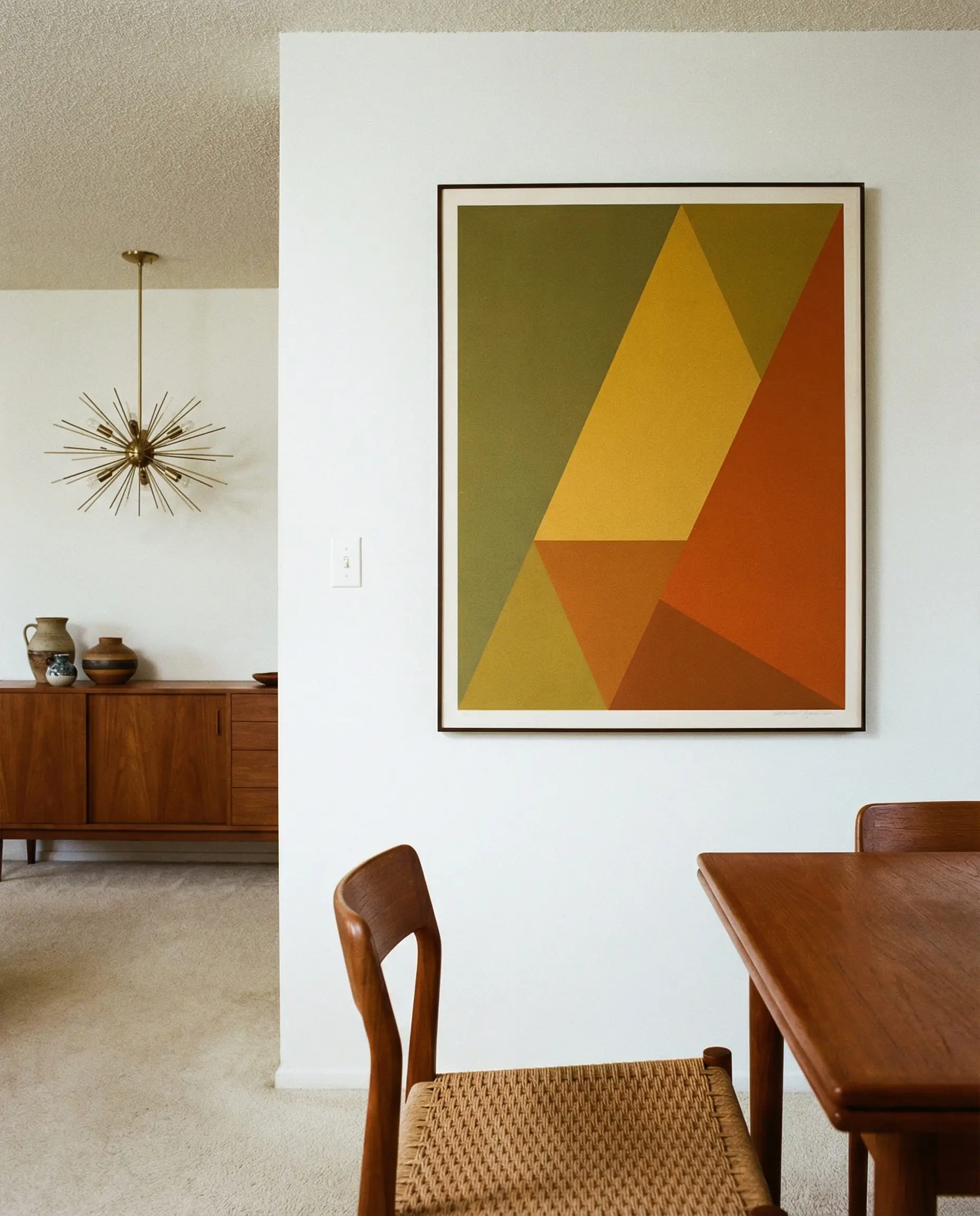 Dining wall featuring a framed art print with bold mid-century shapes in olive and orange.
