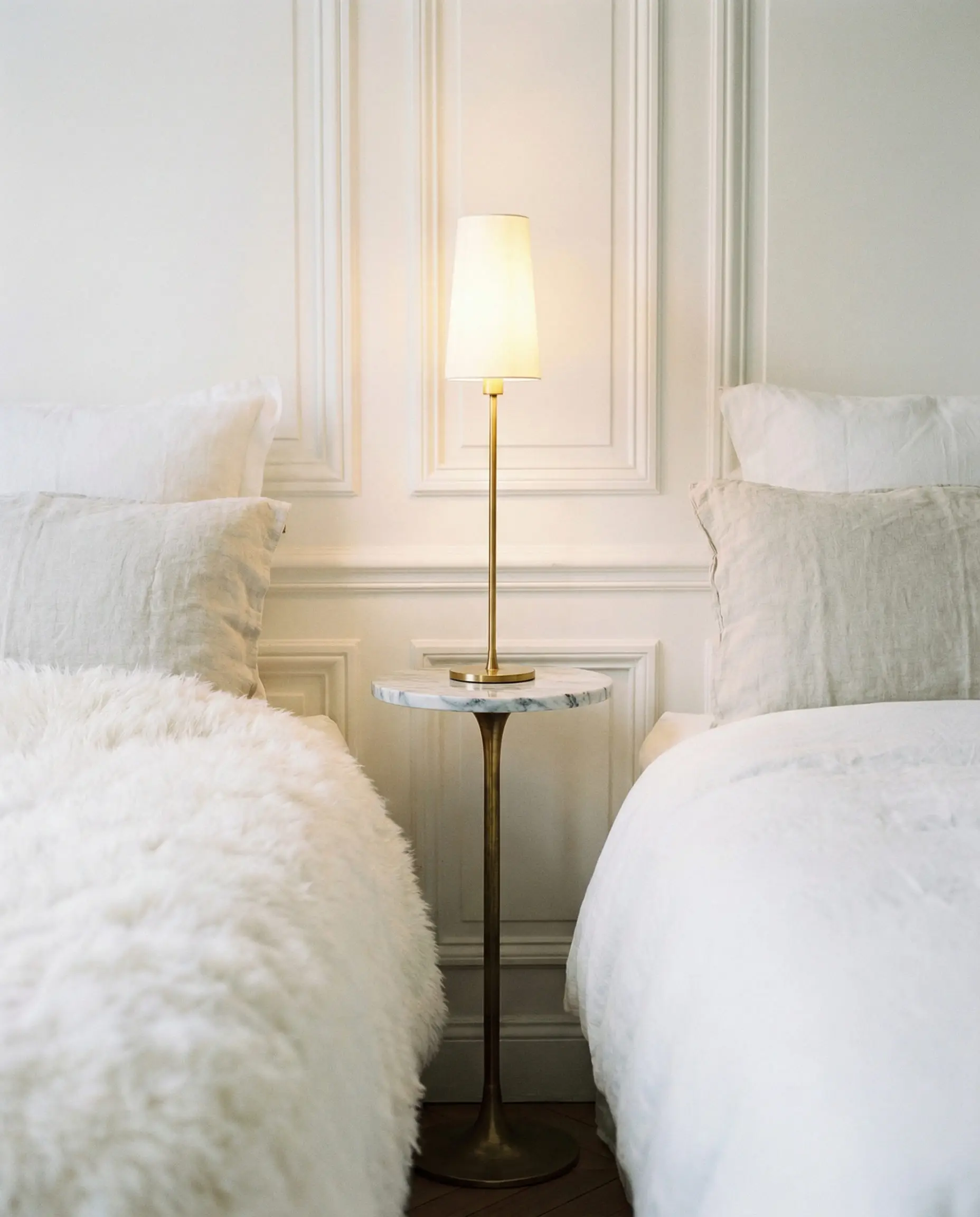 Tiny round pedestal table used as a space-saving nightstand next to a plush bed.