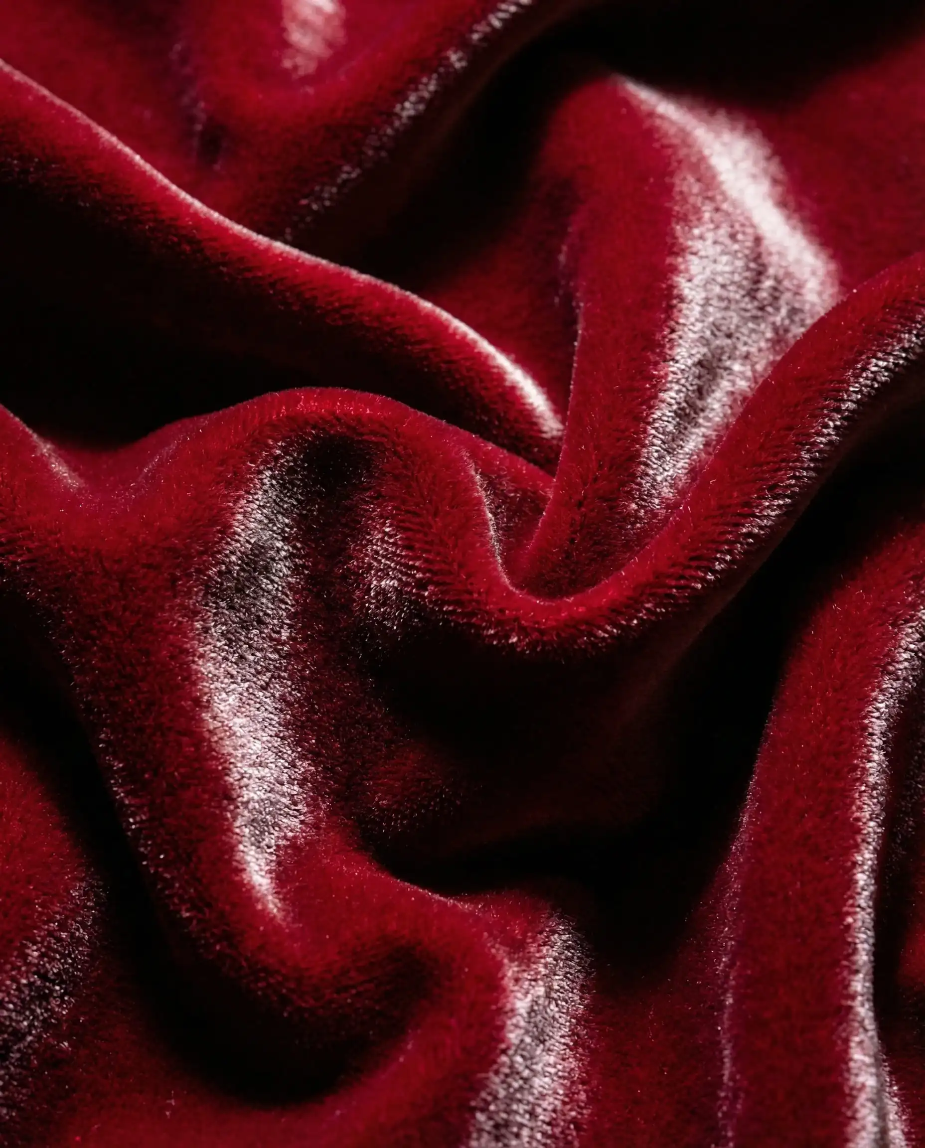 Close-up texture of deep ruby red velvet fabric showing plush pile and light reflection in the folds.