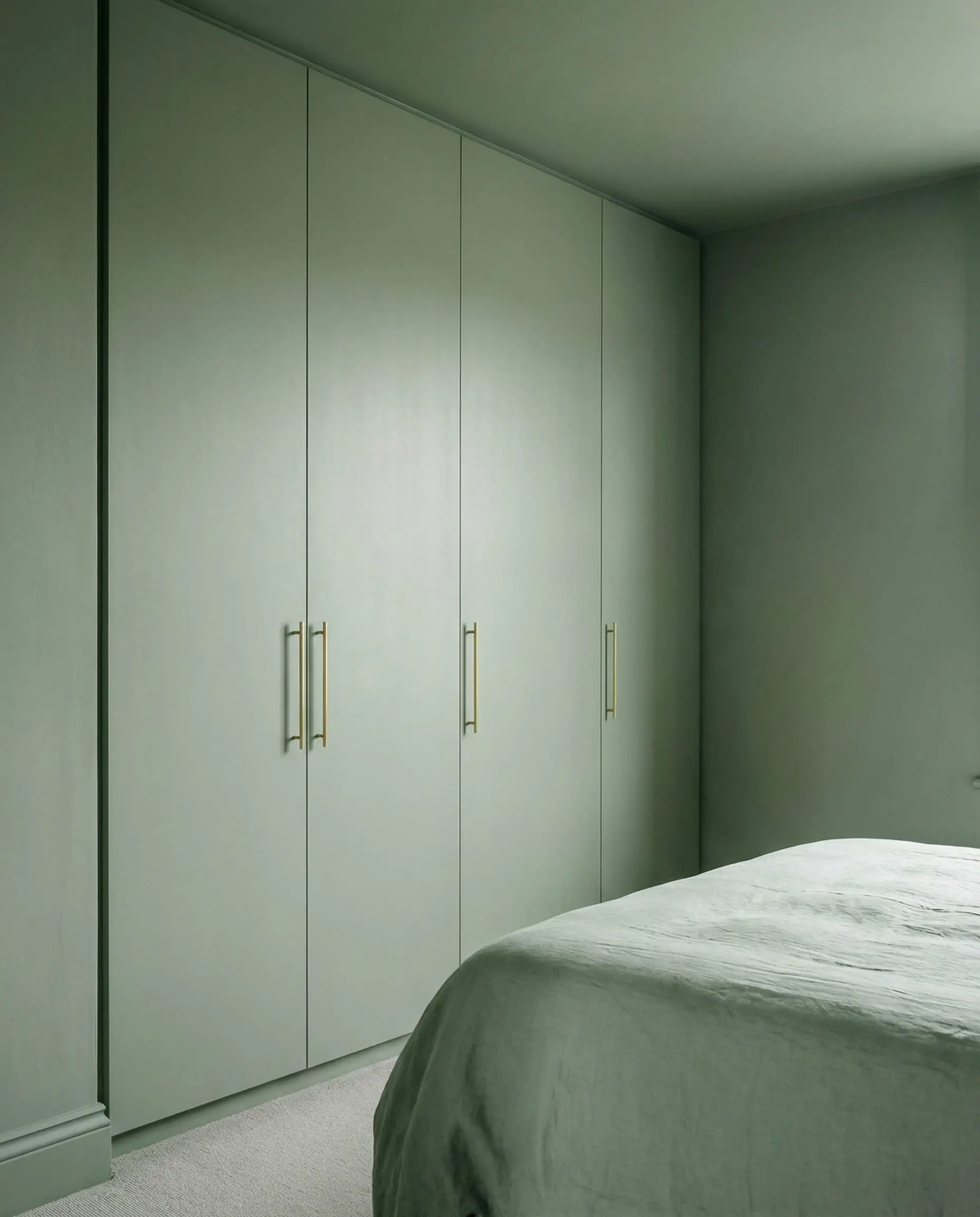 Floor-to-ceiling built-in wardrobes painted sage green to match the walls for an invisible look.