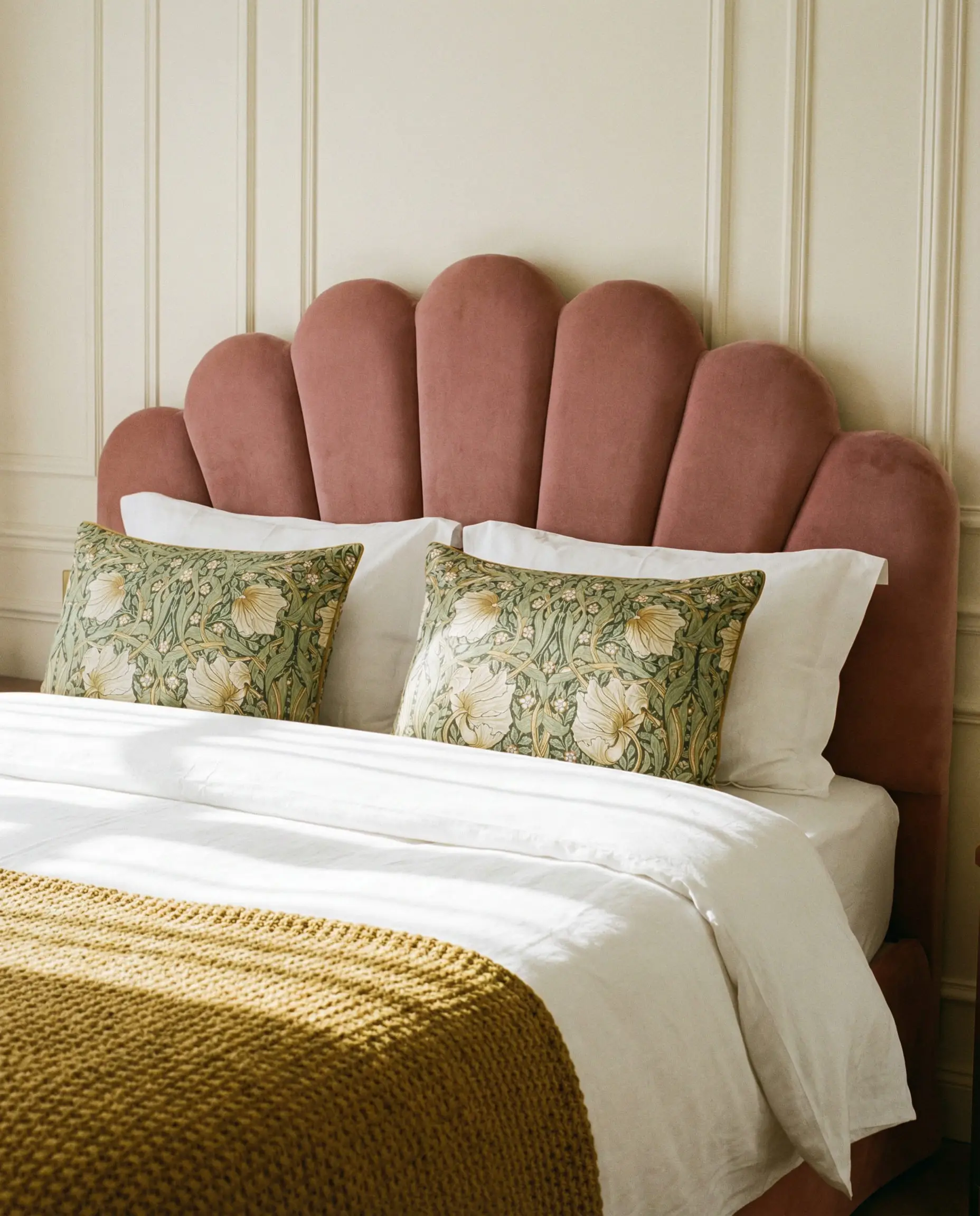 Dusty rose pink velvet headboard with a scalloped curved edge in a romantic, soft bedroom setting.