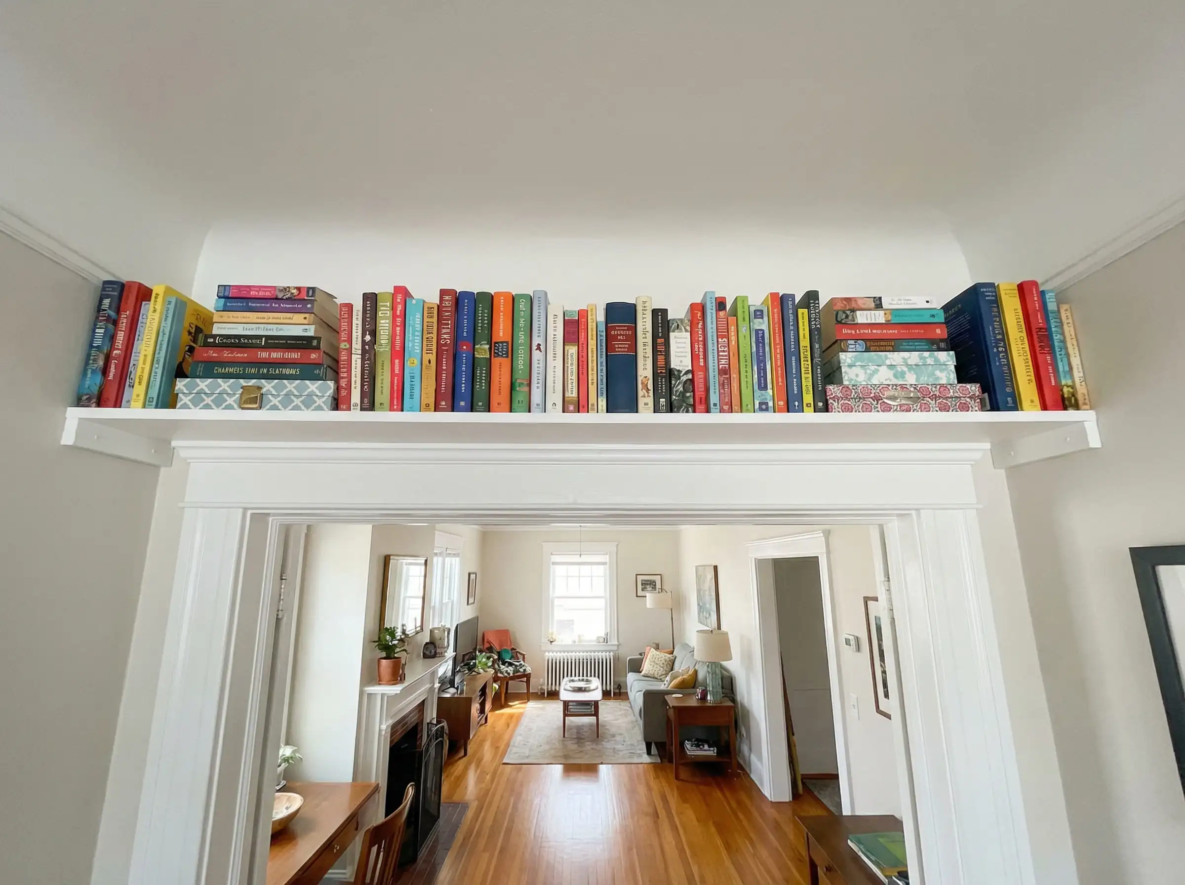 White shelf installed horizontally above a living room door frame holding colorful books.