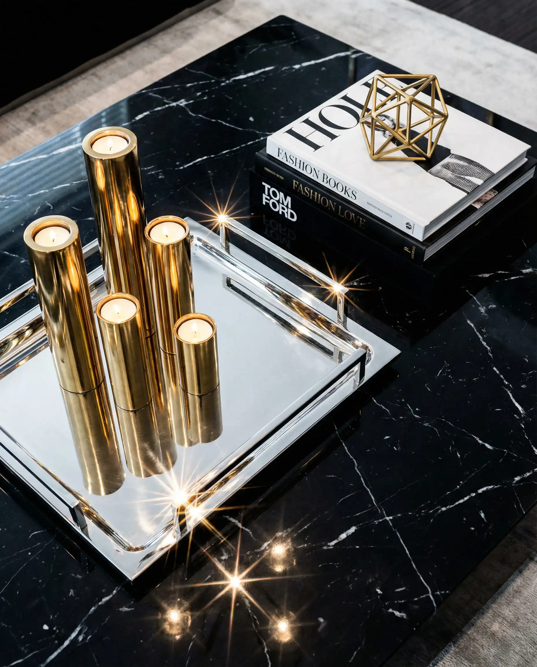 Styled coffee table with a silver chrome tray holding gold candle holders on black marble.