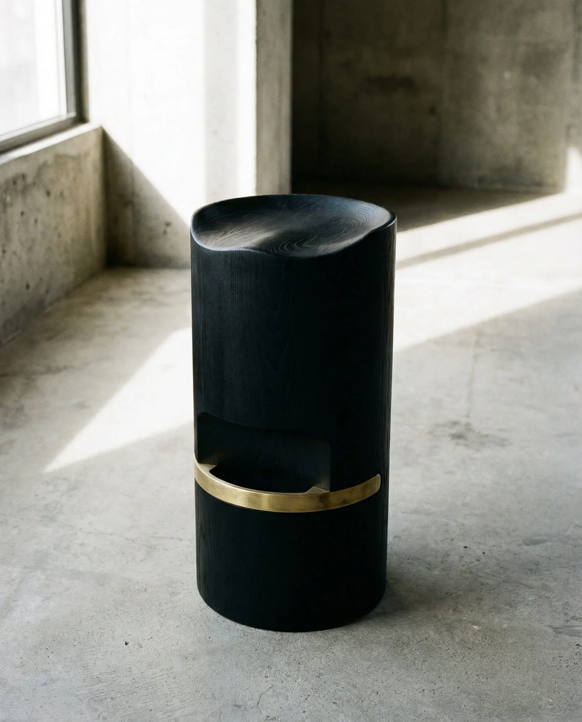 Sculptural solid black wood bar stool with a simple brass footrest ring.