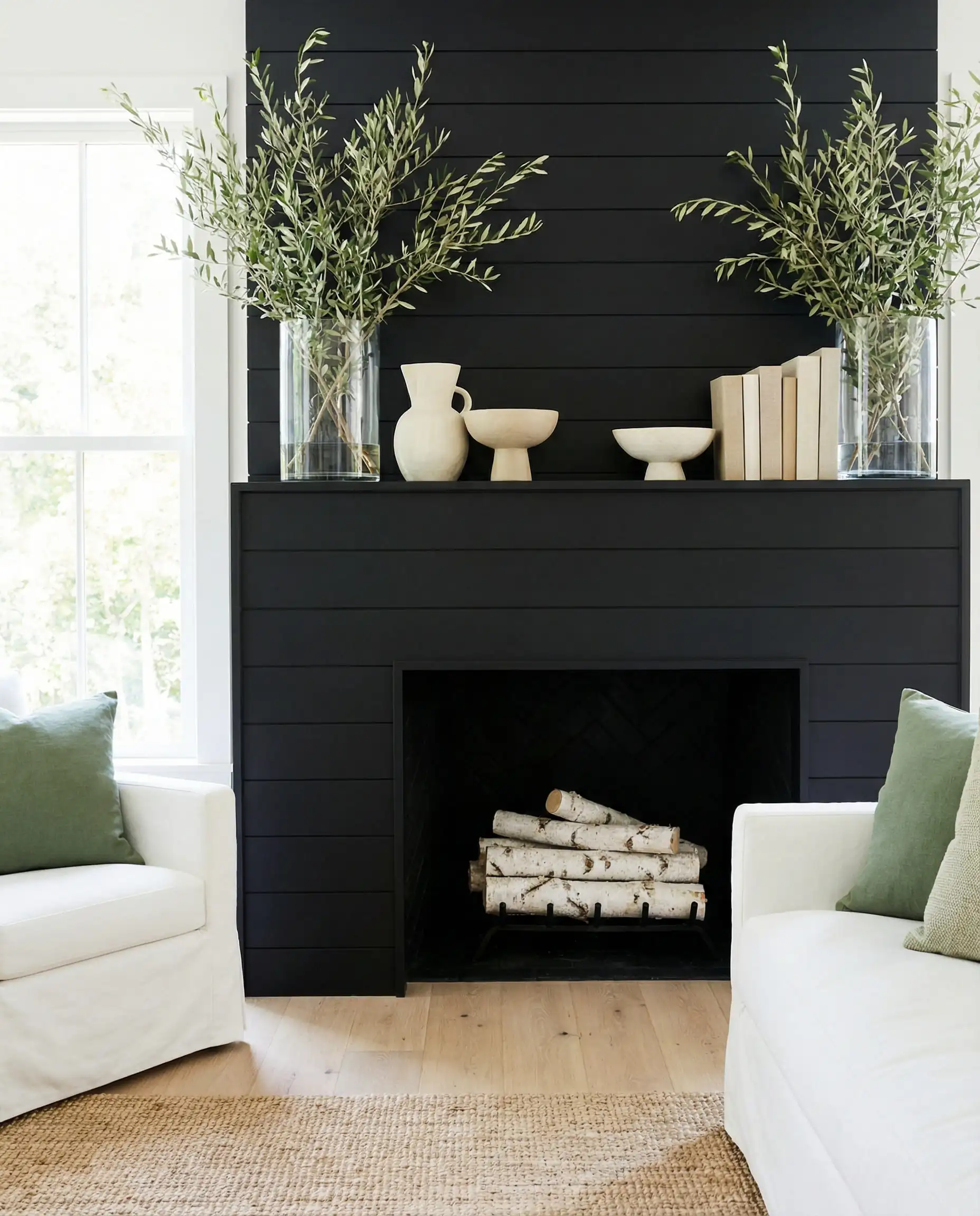 Black fireplace styled with fresh green olive branches and light pottery for spring.