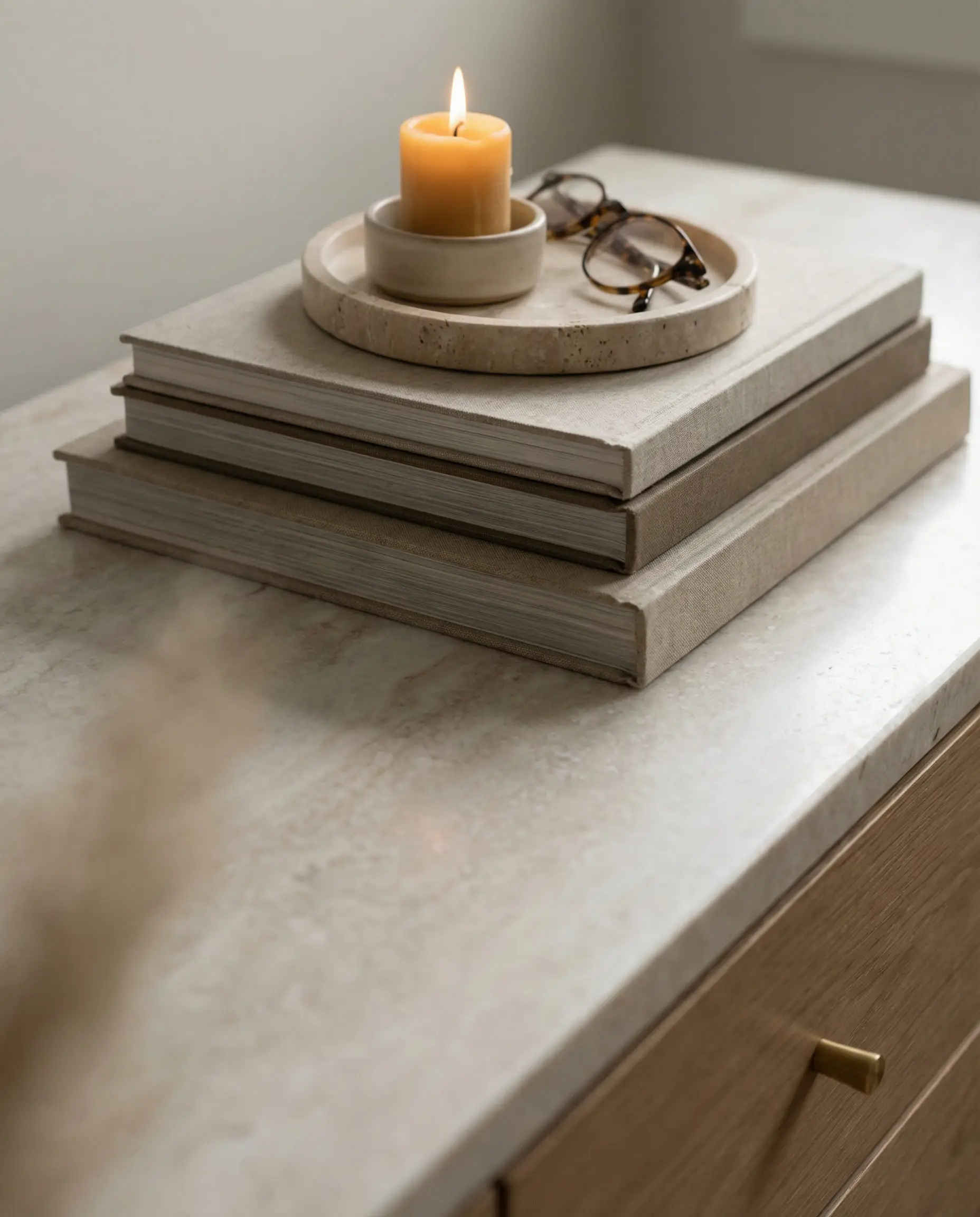 Close up macro shot of sideboard styling with coffee table books, a candle and a stone tray.