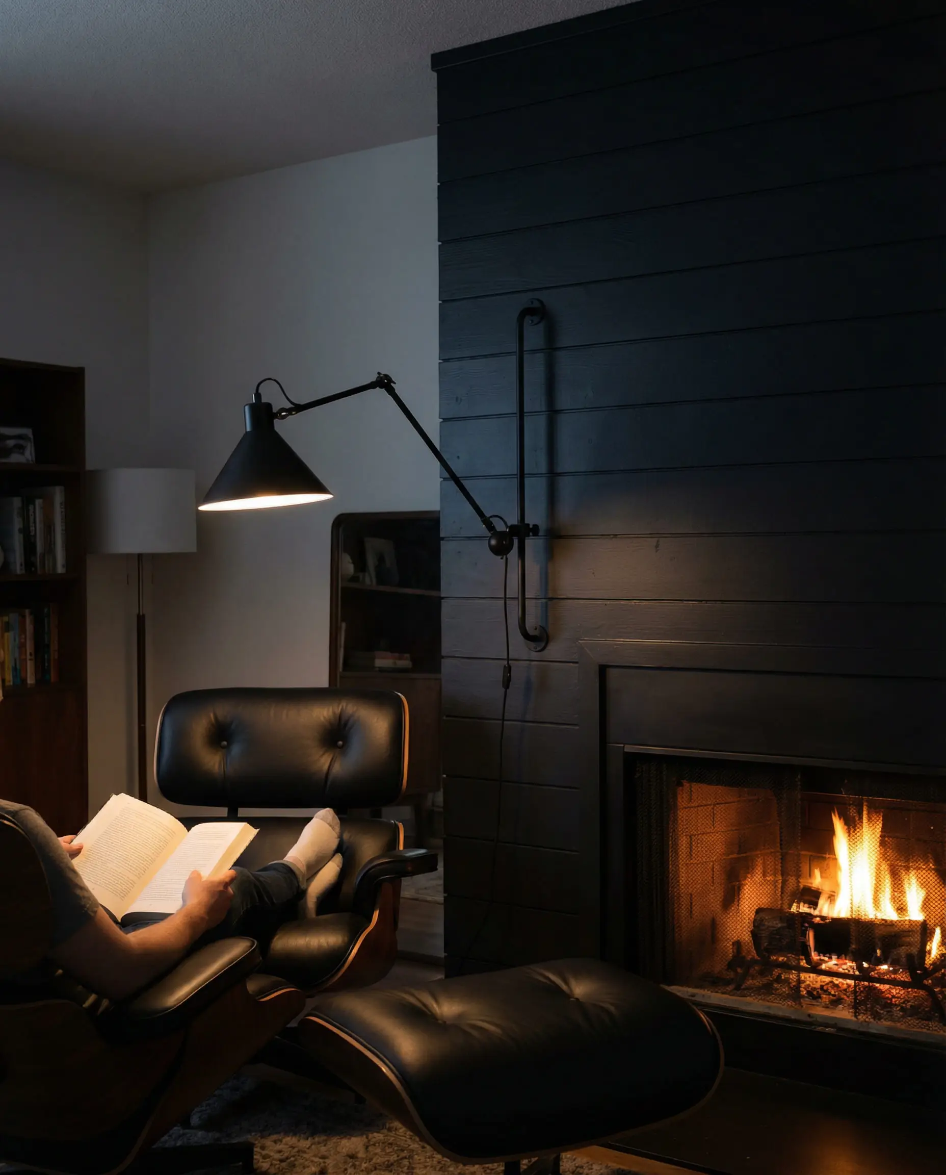 Industrial black swing arm lamp mounted on shiplap above a reading chair.