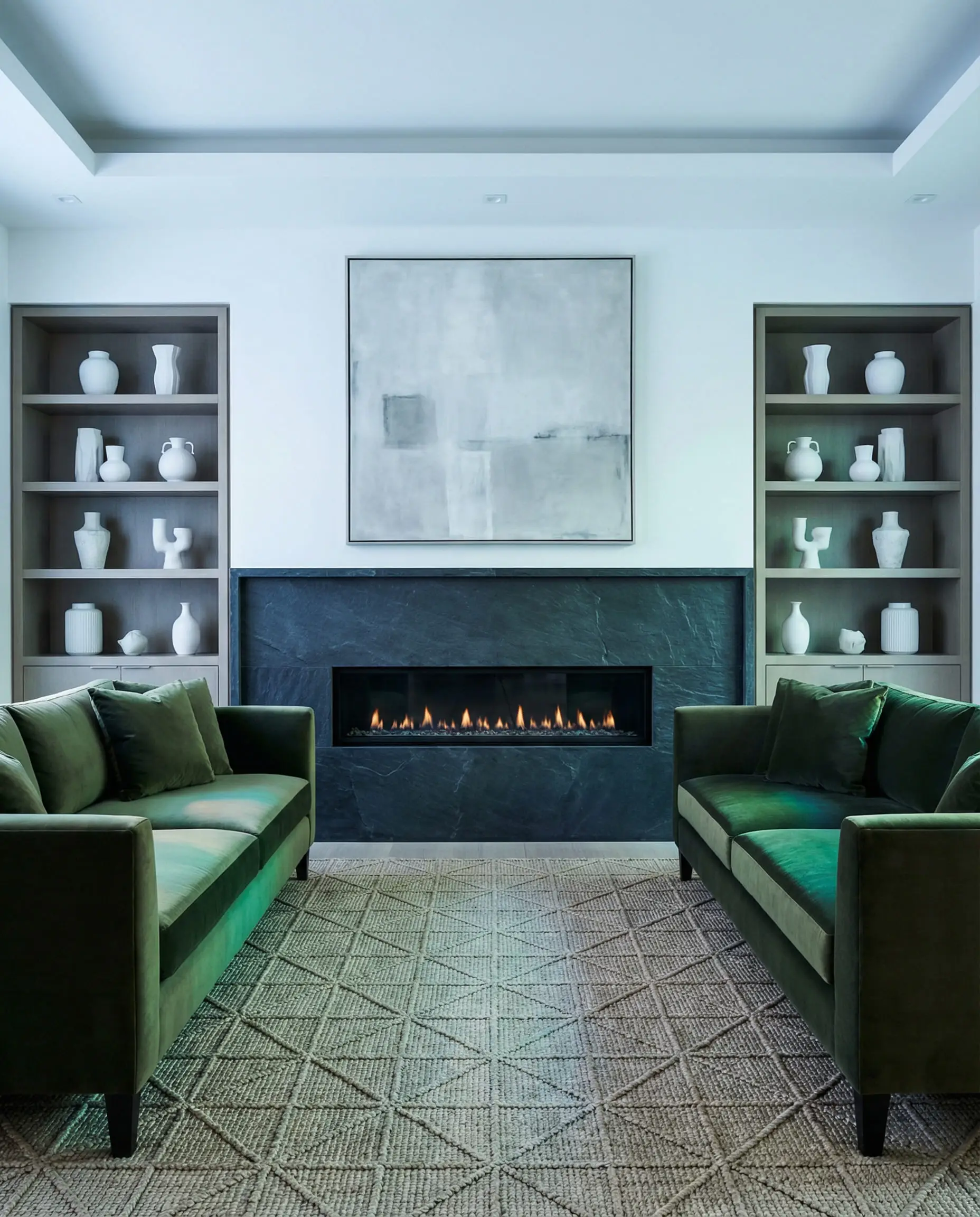 Perfectly symmetrical living room design with two olive green velvet sofas flanking a modern fireplace and abstract art.