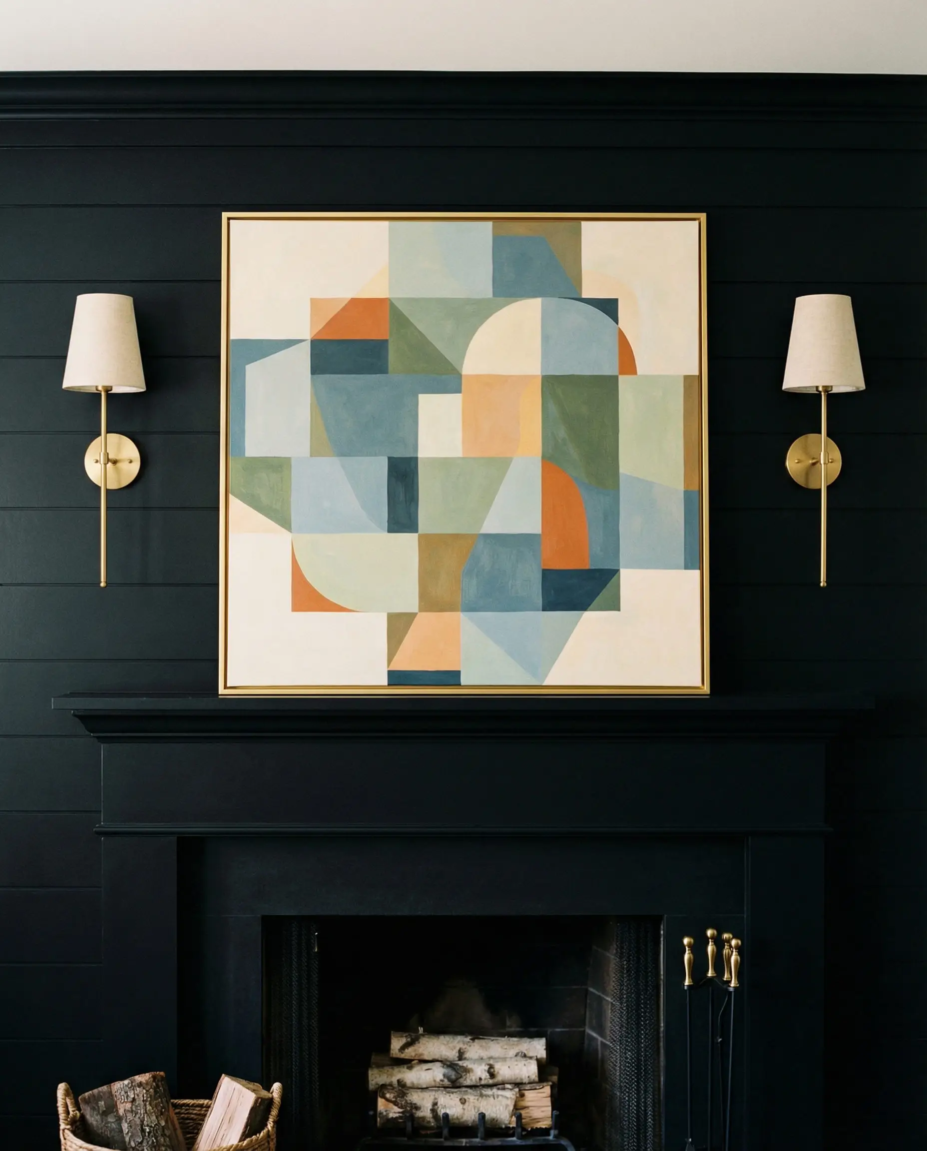 Two brass sconces symmetrically flanking art on a black shiplap fireplace.