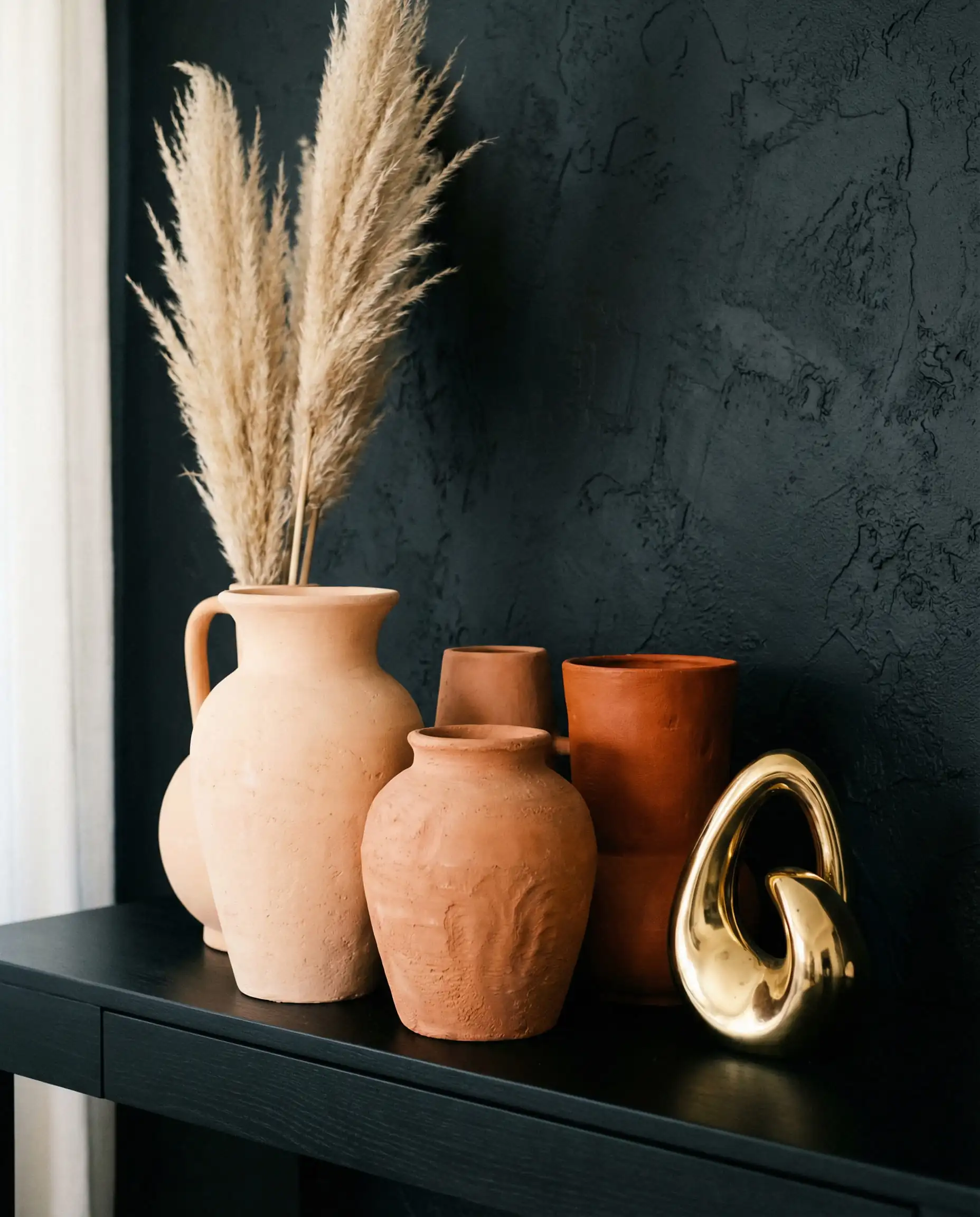 Vignette of handmade terracotta clay vases and gold sculptures on a black console table.