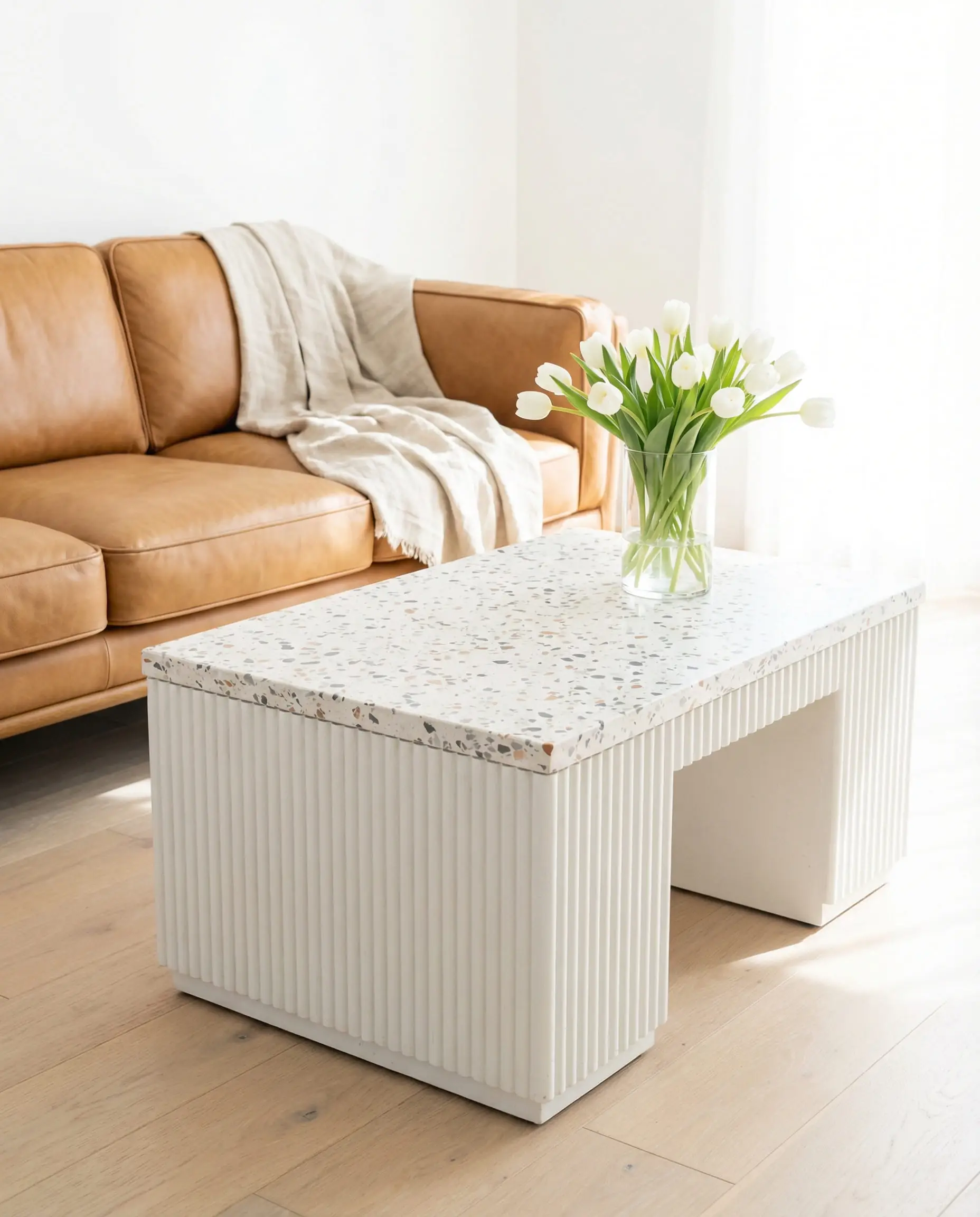 White terrazzo coffee table with fluted sides styled in a bright California modern living room with a caramel leather sofa.