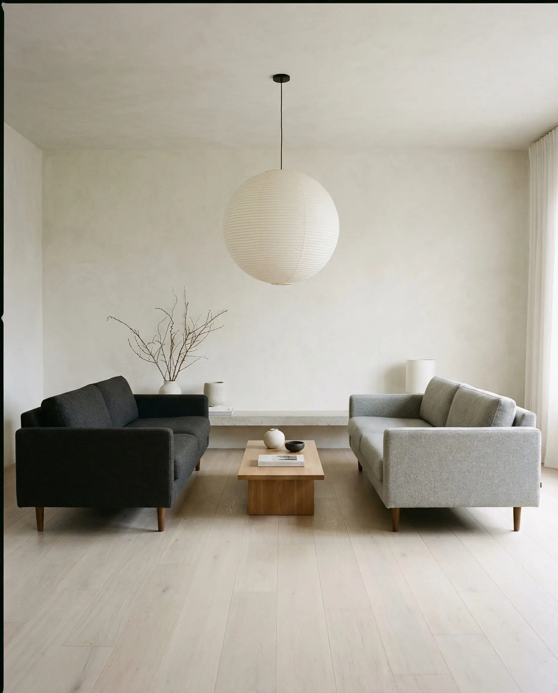 Minimalist living room with two track-arm sofas, one in dark charcoal wool and the other in light heather grey.