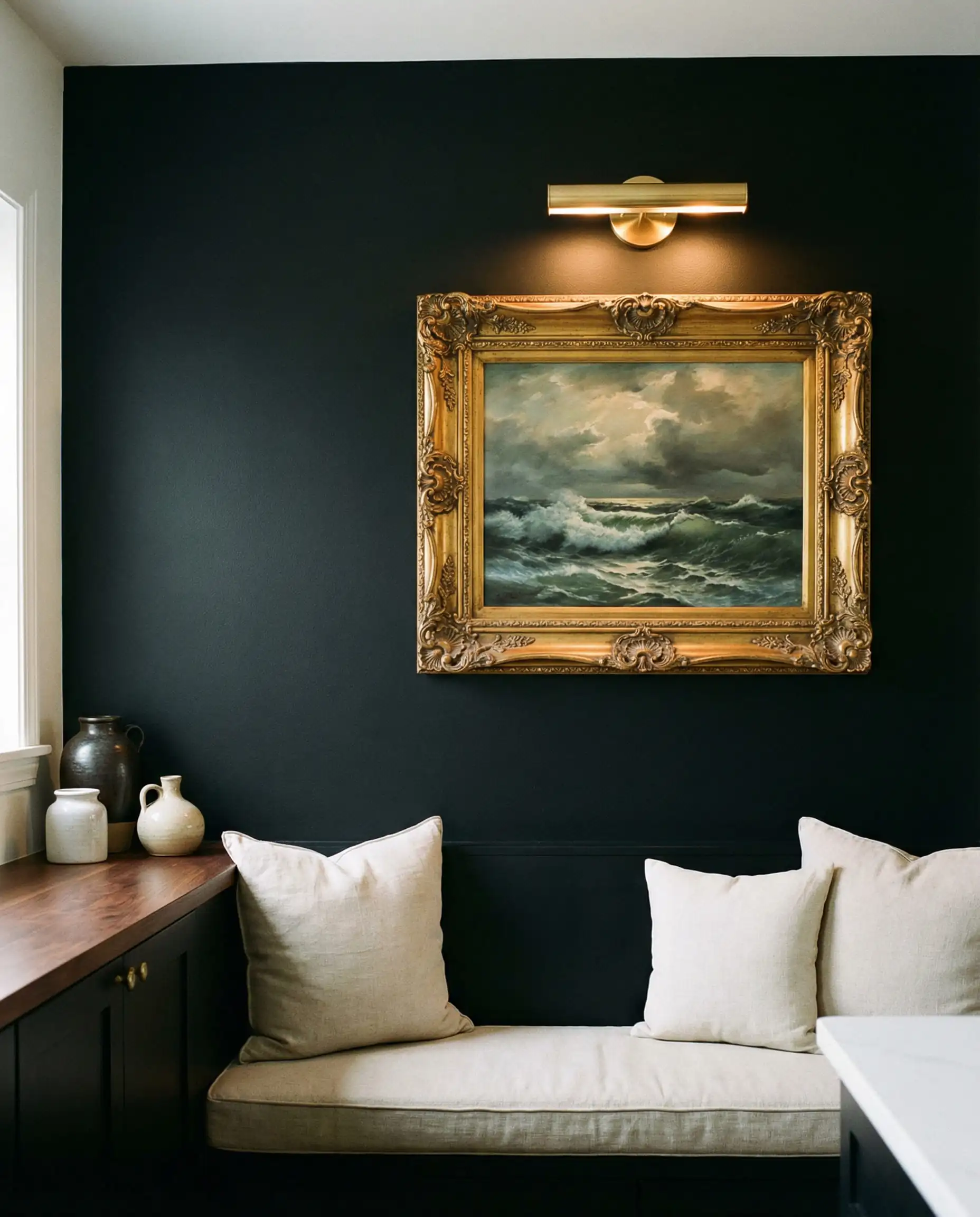 Vintage oil painting in an ornate antique gold frame hanging on a matte black kitchen wall.