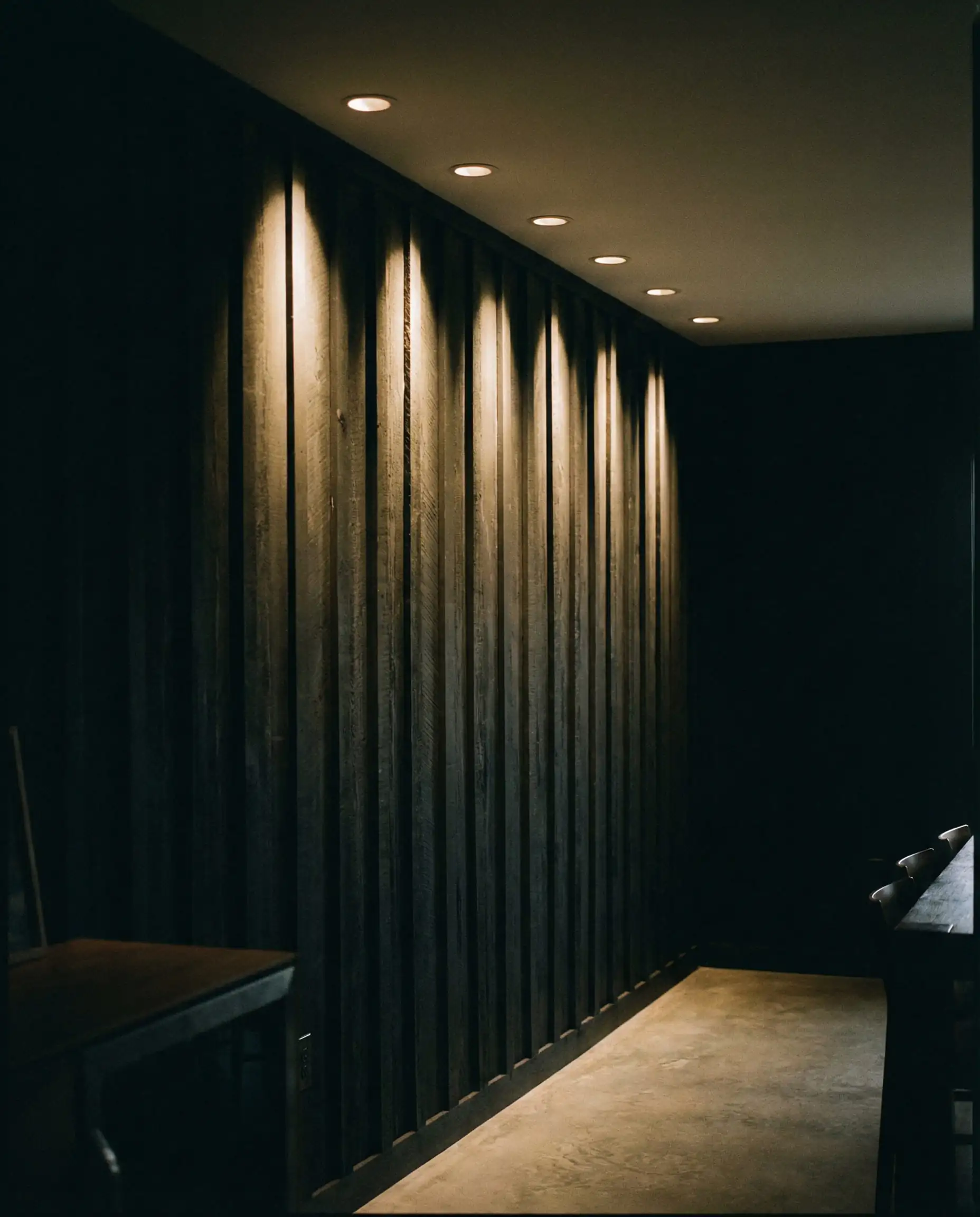 Recessed ceiling lights casting grazing light down a black shiplap wall to highlight texture.