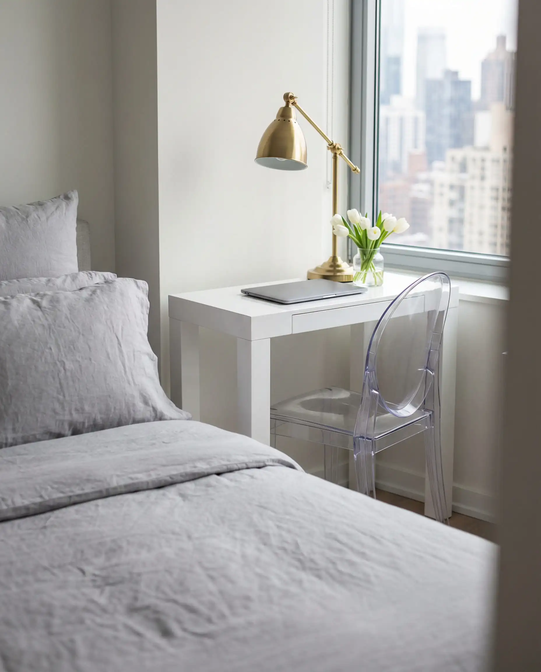 Small bedroom hack using a sleek white desk as a bedside table with a ghost chair.