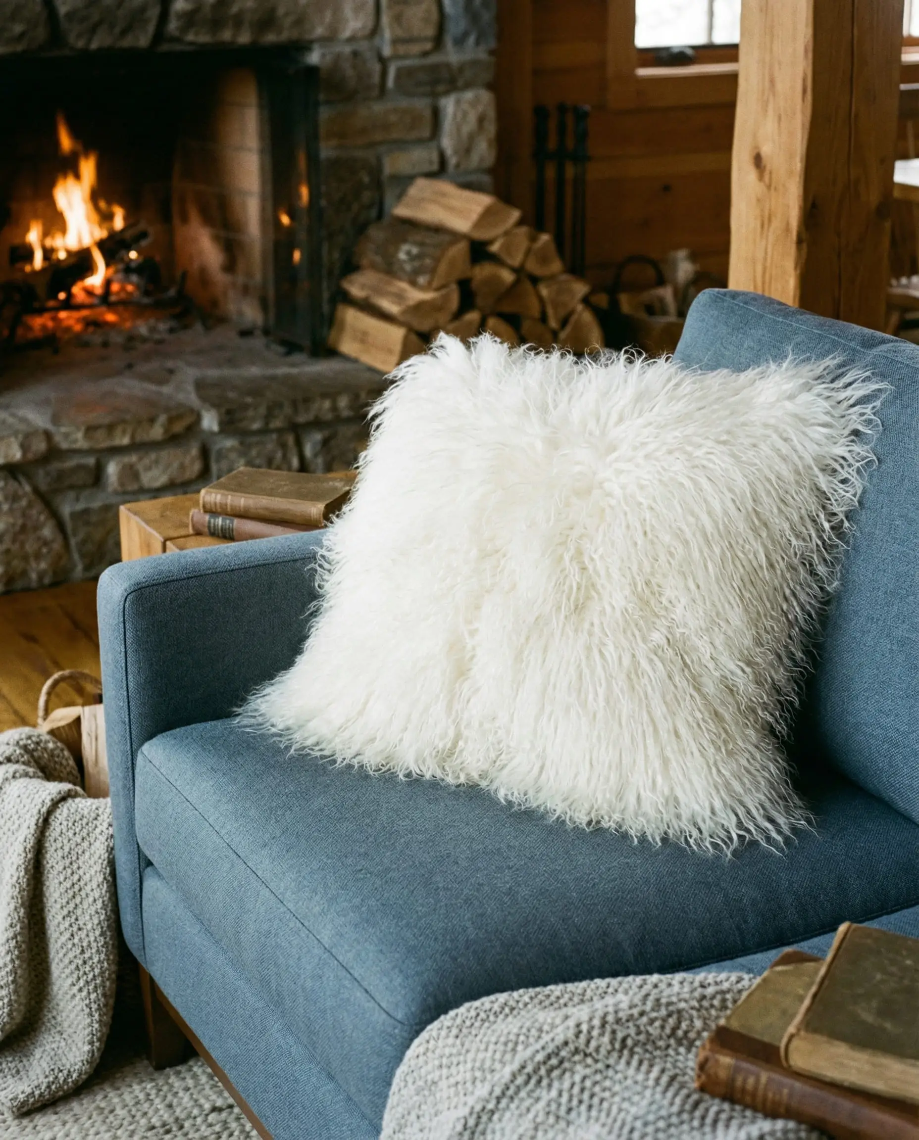 A white Mongolian sheepskin faux fur pillow resting on a tailored slate blue wool couch.