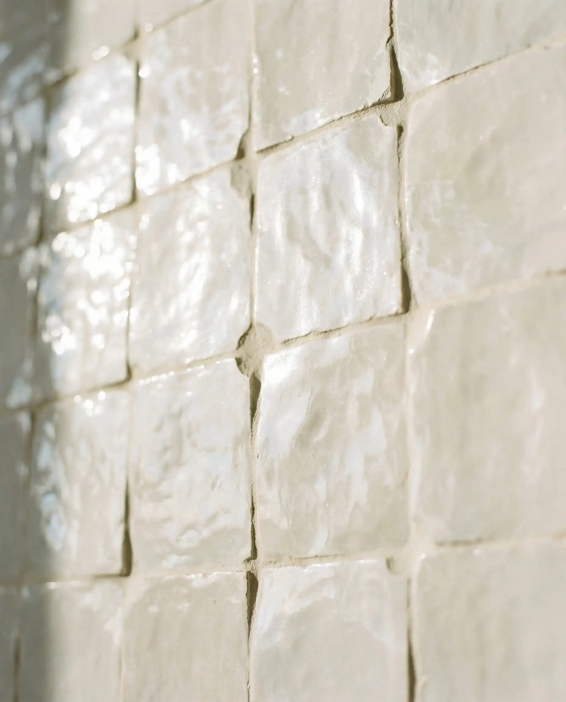 Macro detail of handcrafted white Zellige tiles showing uneven texture and pearlescent glaze.