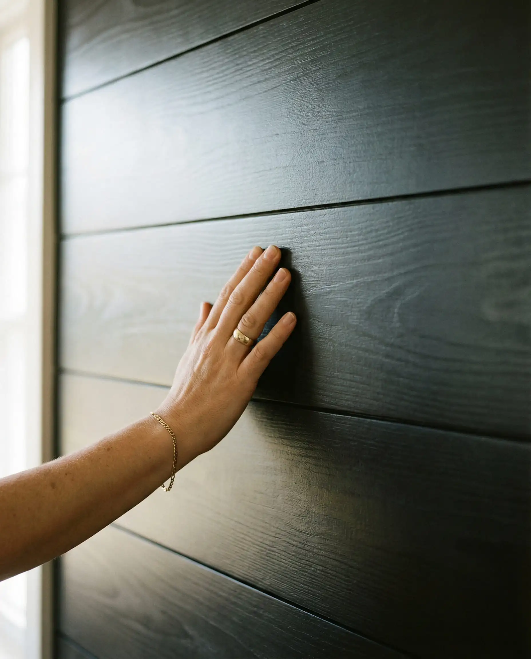 Close-up detail of 8-inch wide plank horizontal black shiplap with a hand for scale contrast.