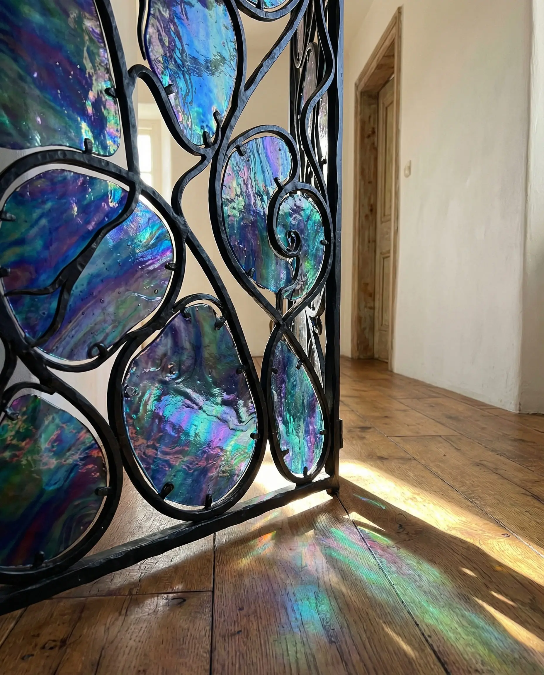 Detail of an Art Nouveau room divider featuring black wrought iron vines and iridescent Favrile glass panels in blue and green.