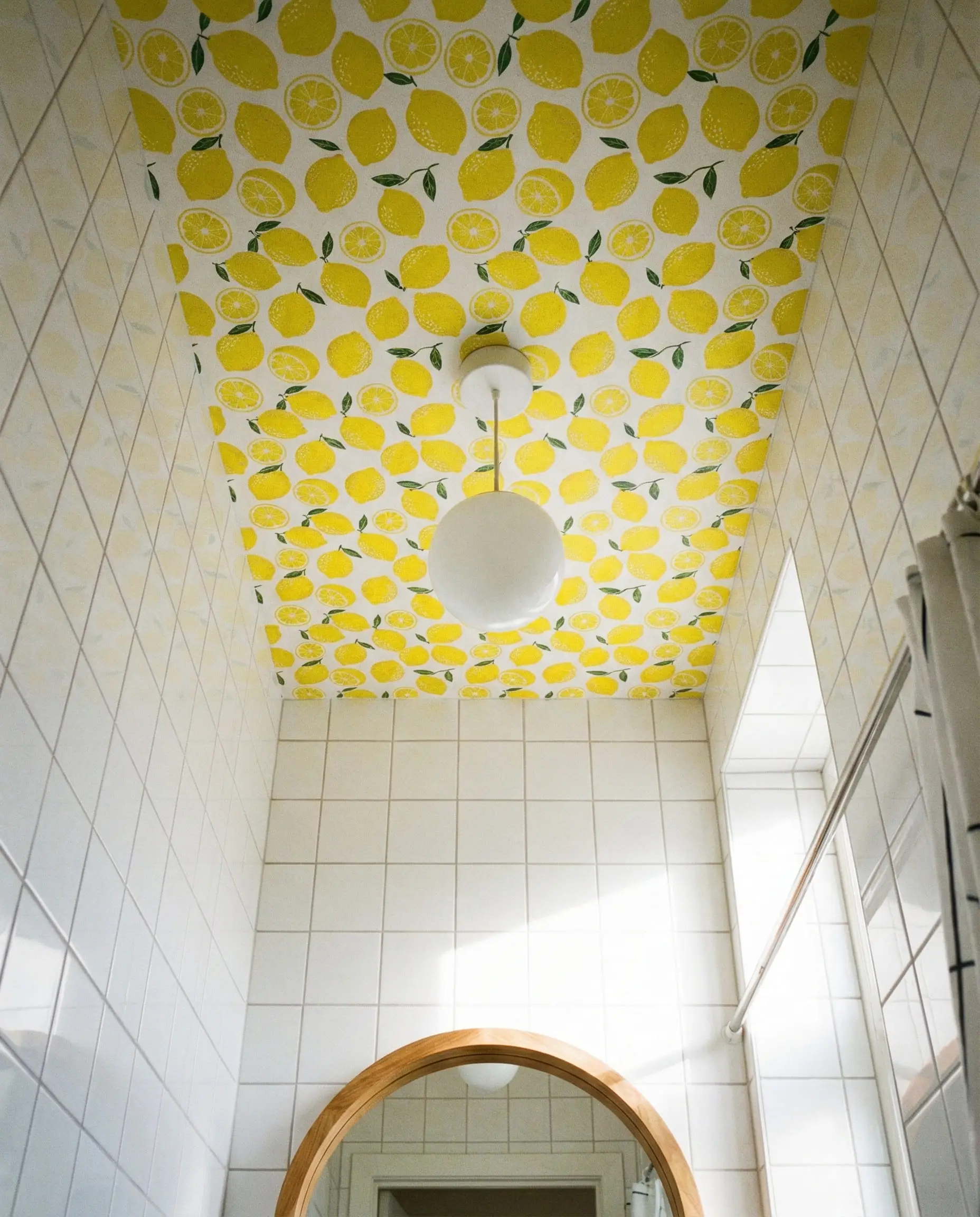 White tiled bathroom with a vibrant lemon yellow wallpapered ceiling.