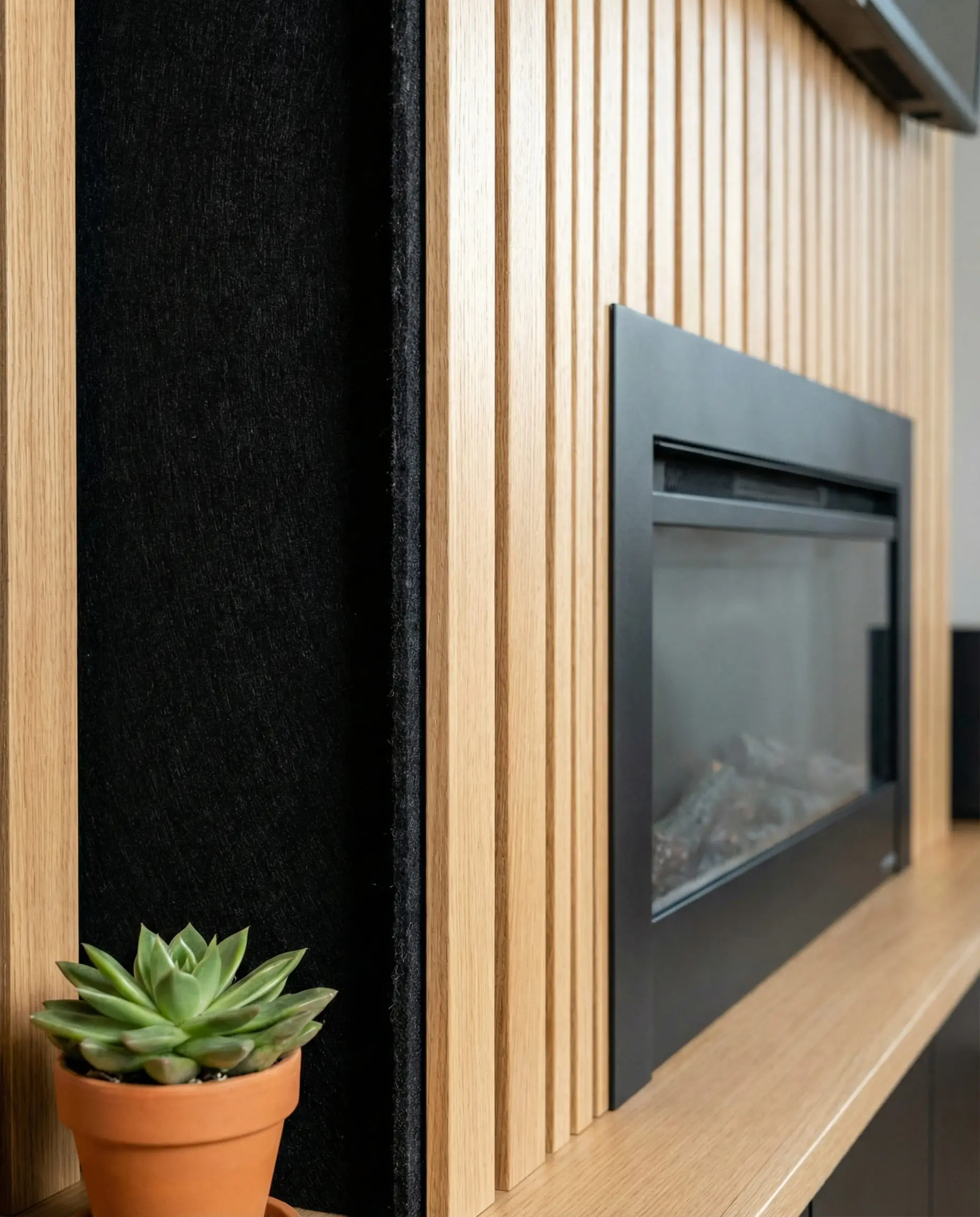 Macro detail of oak wood slats on black acoustic felt backing, installed around a modern electric fireplace.