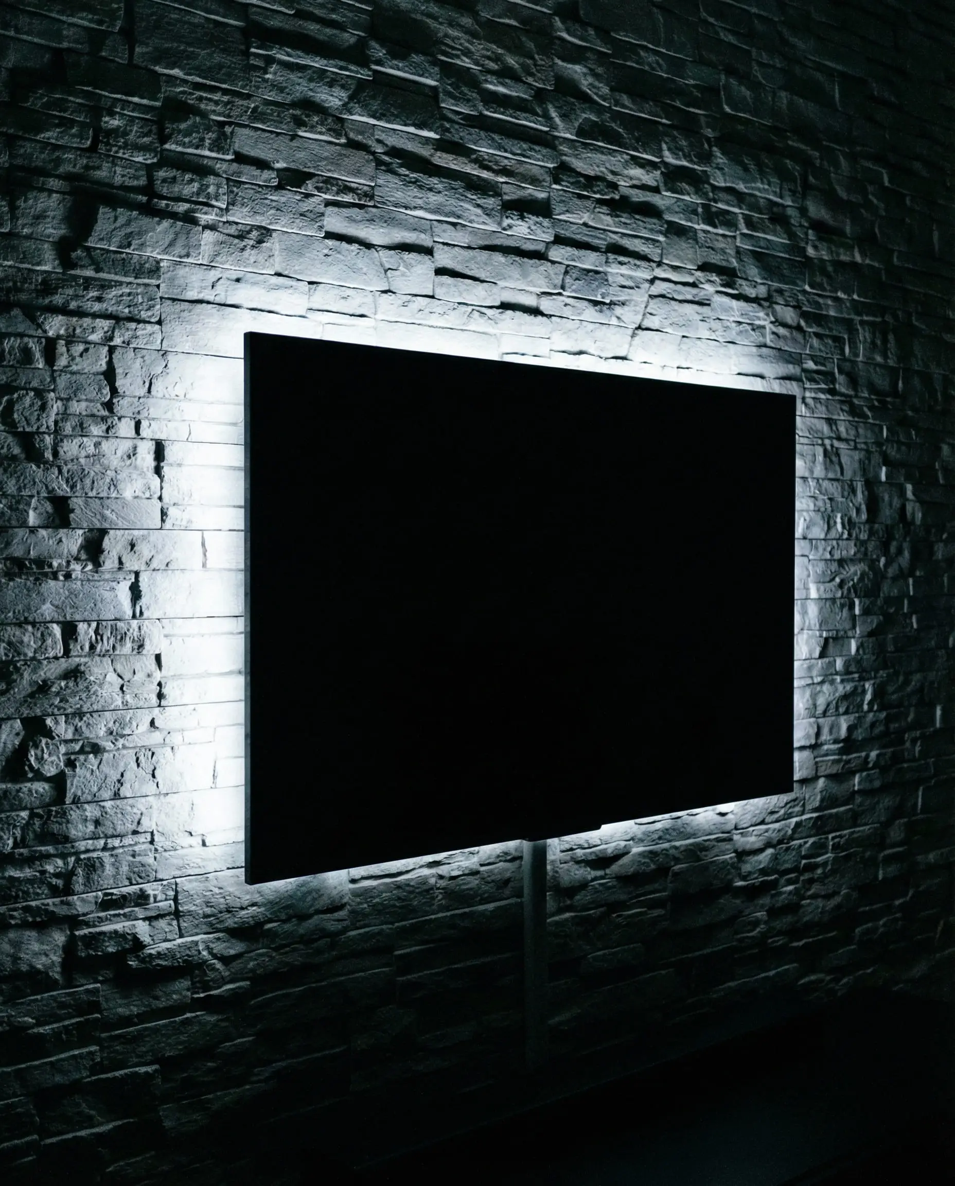 Dark room with LED bias lighting glowing behind a wall-mounted TV on a stone wall.