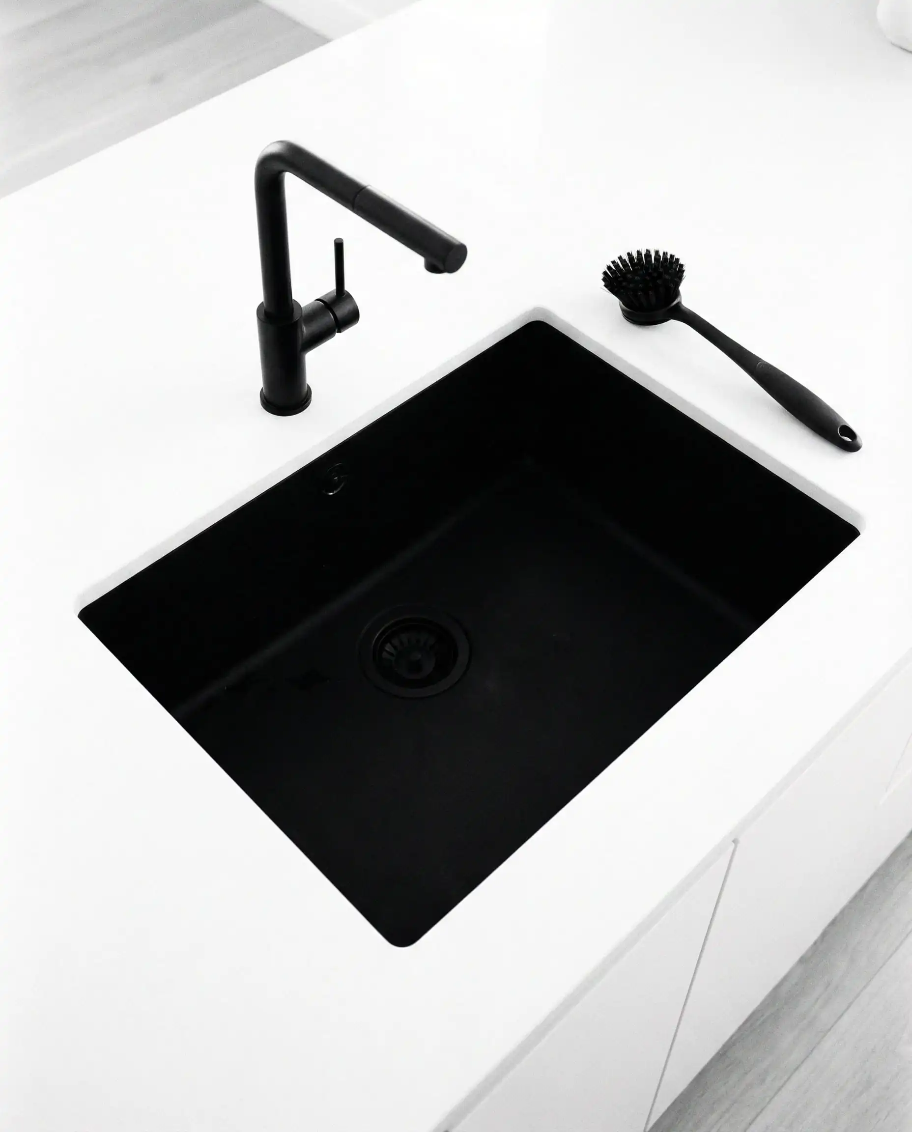 Top-down view of a matte black composite sink and black faucet set into a pure white quartz countertop.
