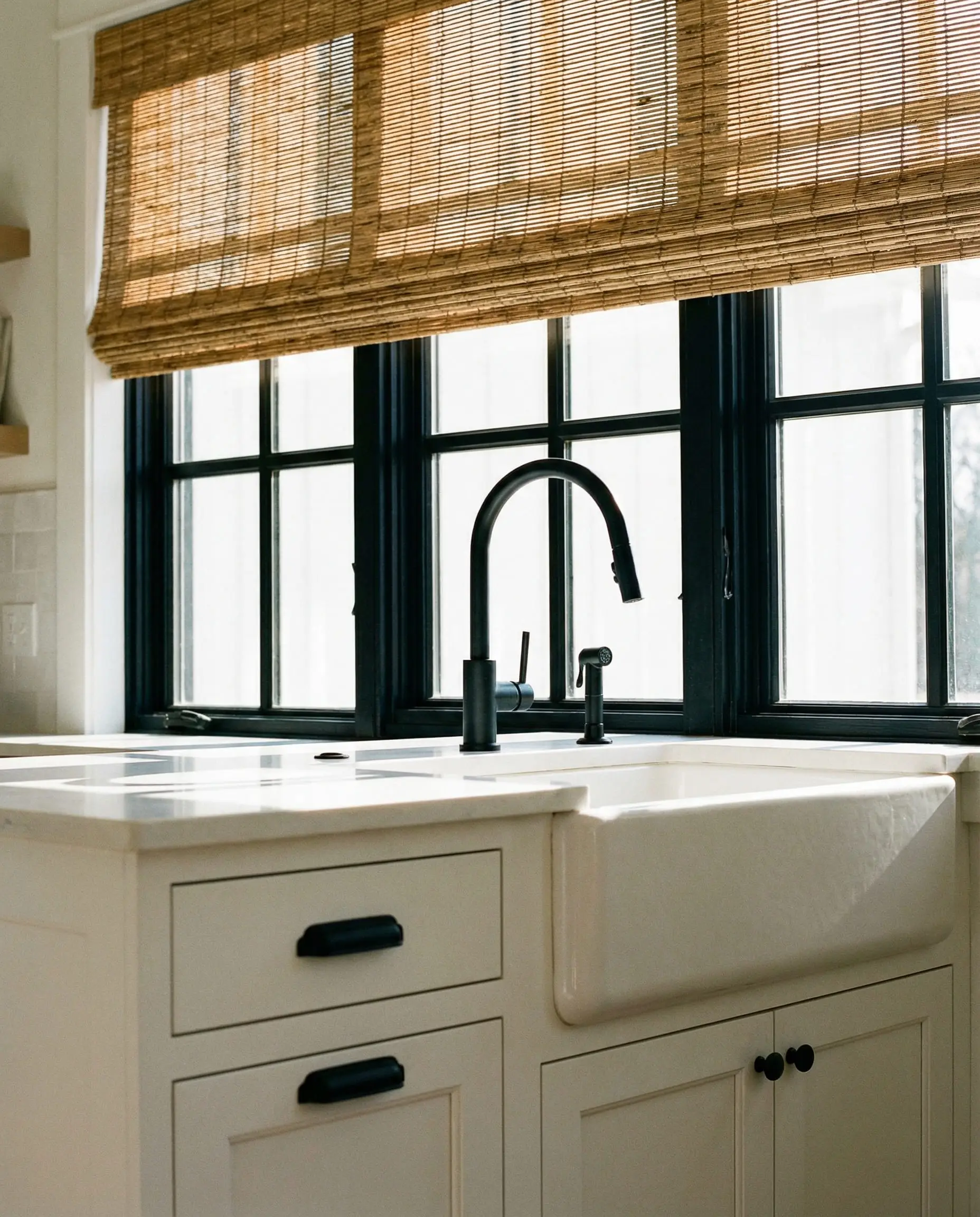 White kitchen sink area with black hardware and matching black window frames.