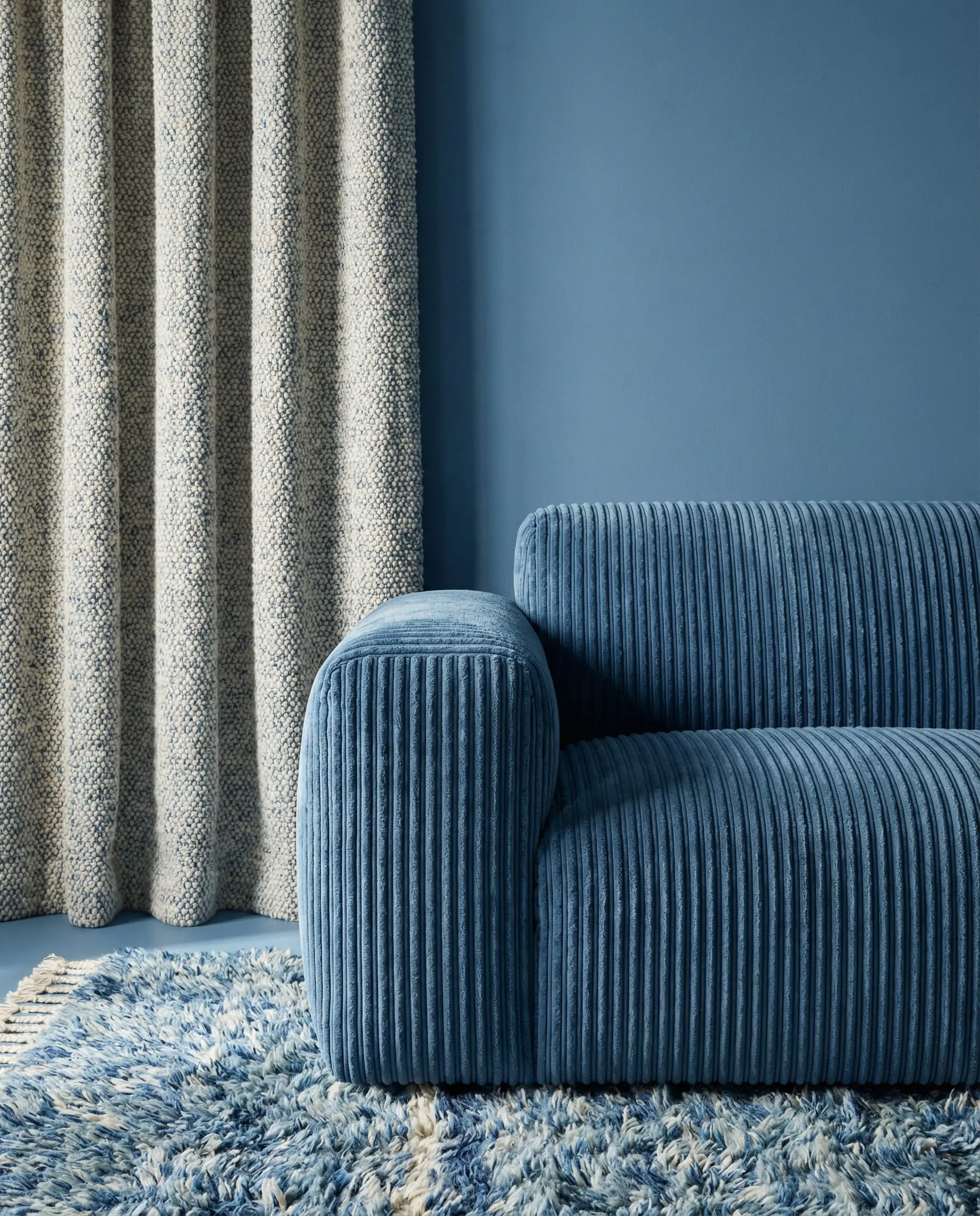 Interior corner showing a mix of blue walls, velvet sofa, and bouclé curtains.
