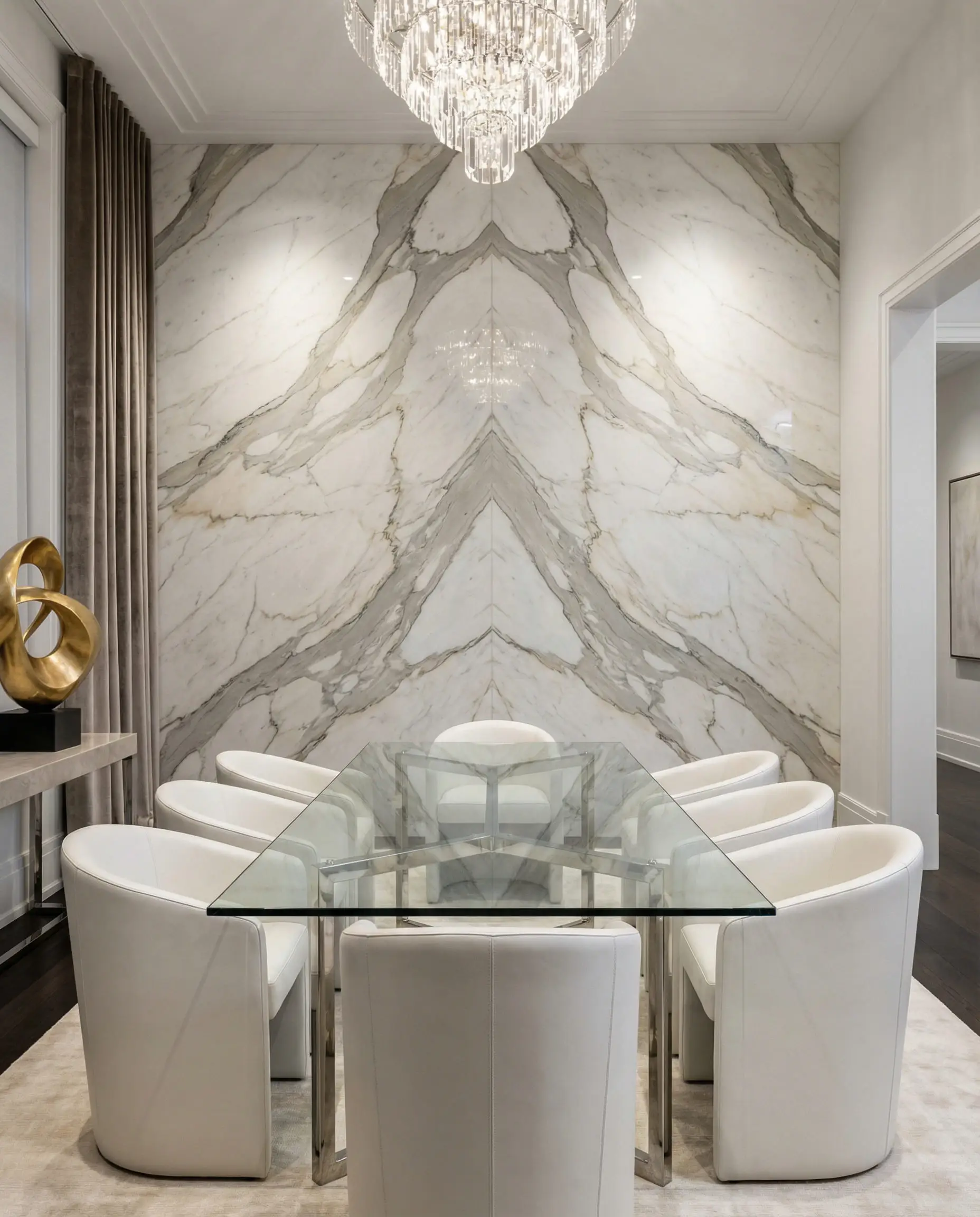 Opulent dining room with a floor-to-ceiling bookmatched Calacatta Gold marble accent wall and glass dining table.