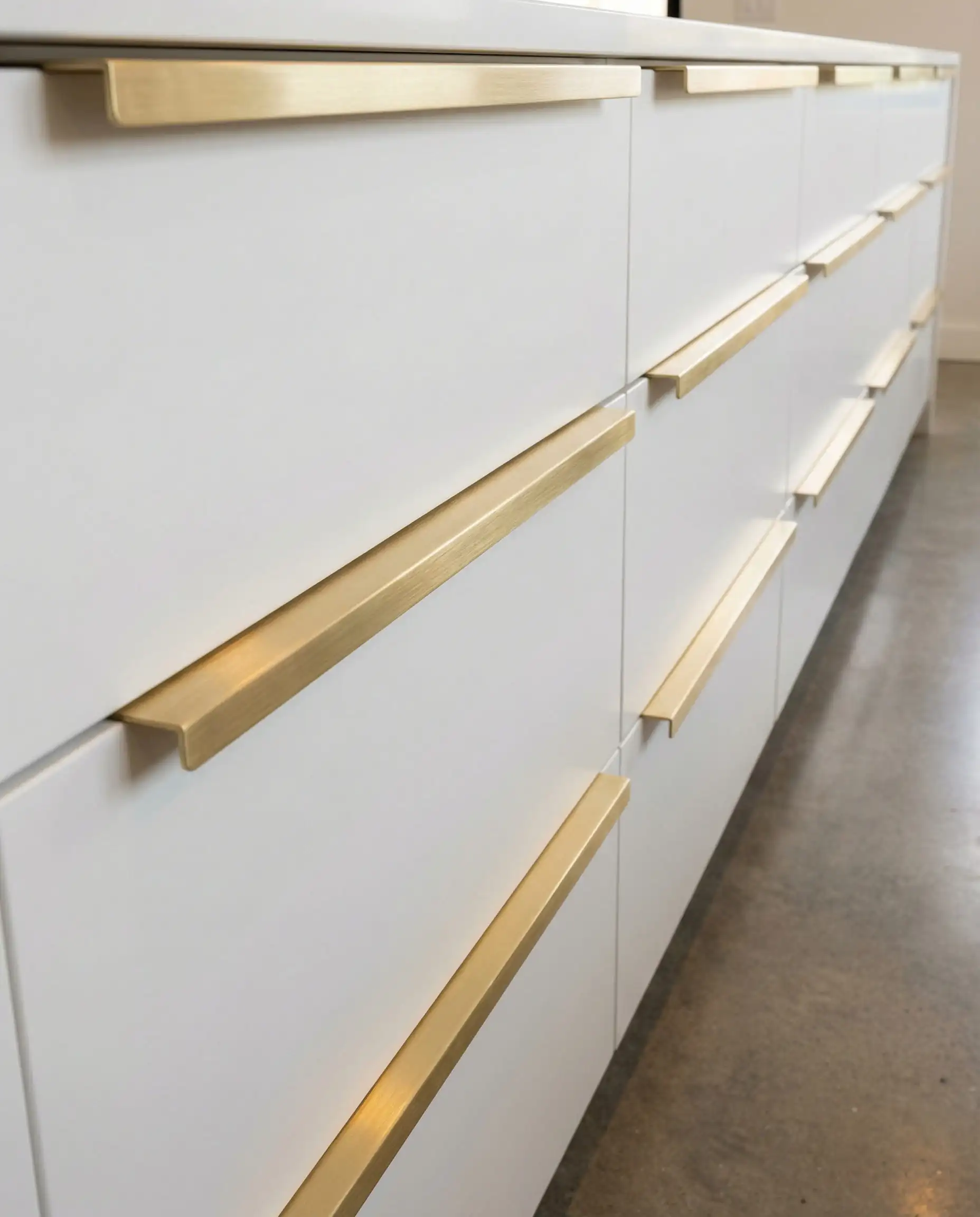 Sleek brushed brass edge pulls on flat-panel modern white kitchen drawers.