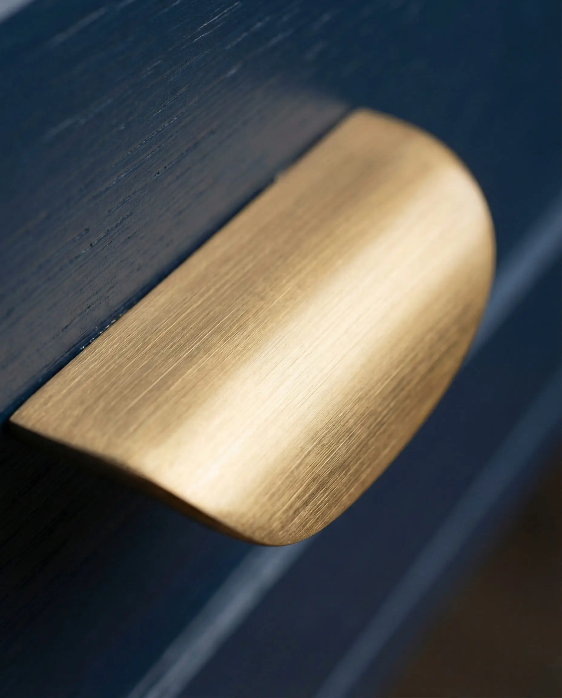 Macro shot of a brushed brass drawer pull against a dark navy blue cabinet surface showing the satin metal texture.