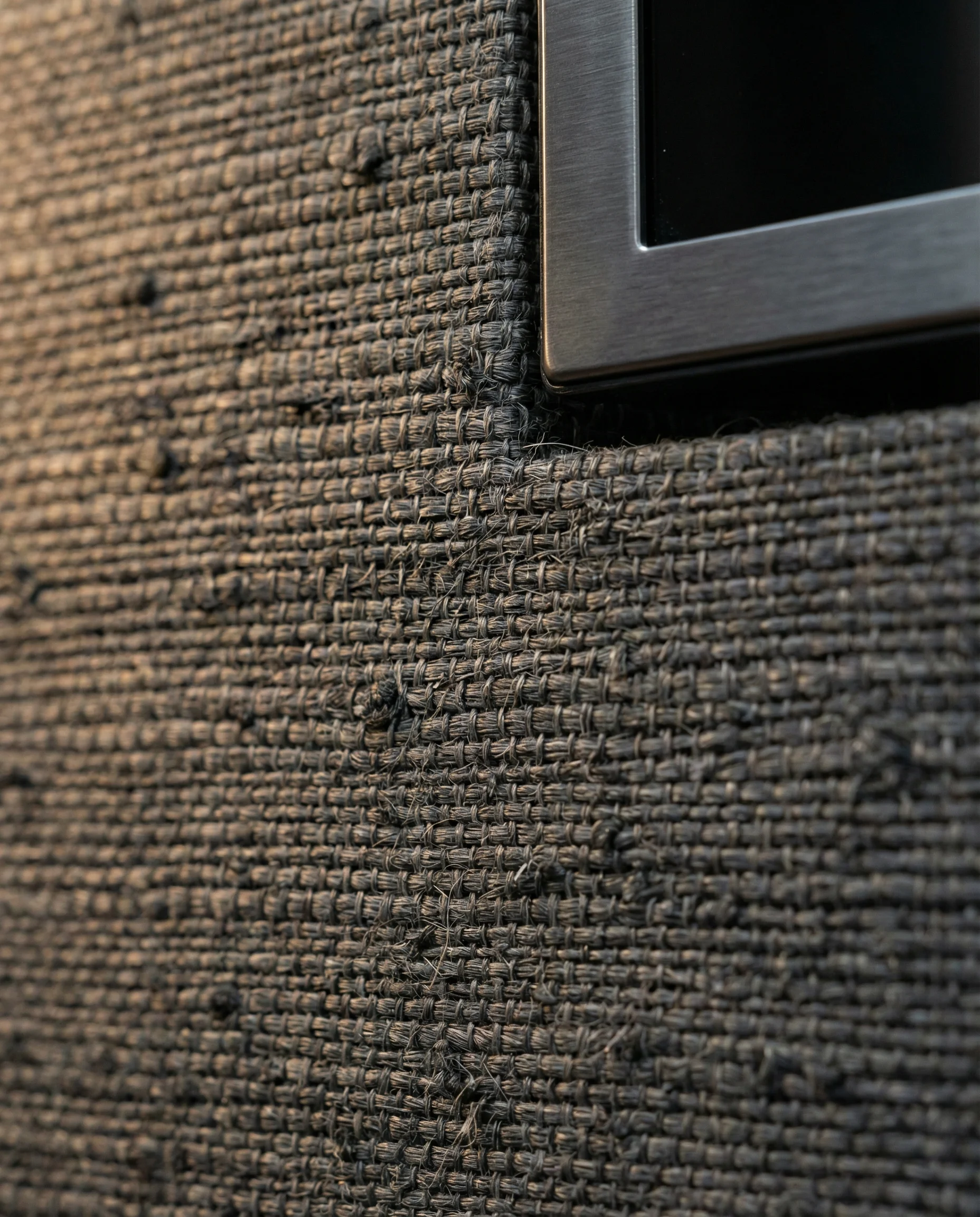 Close-up detail of charcoal grey grasscloth wallpaper texture behind a sleek TV bezel.