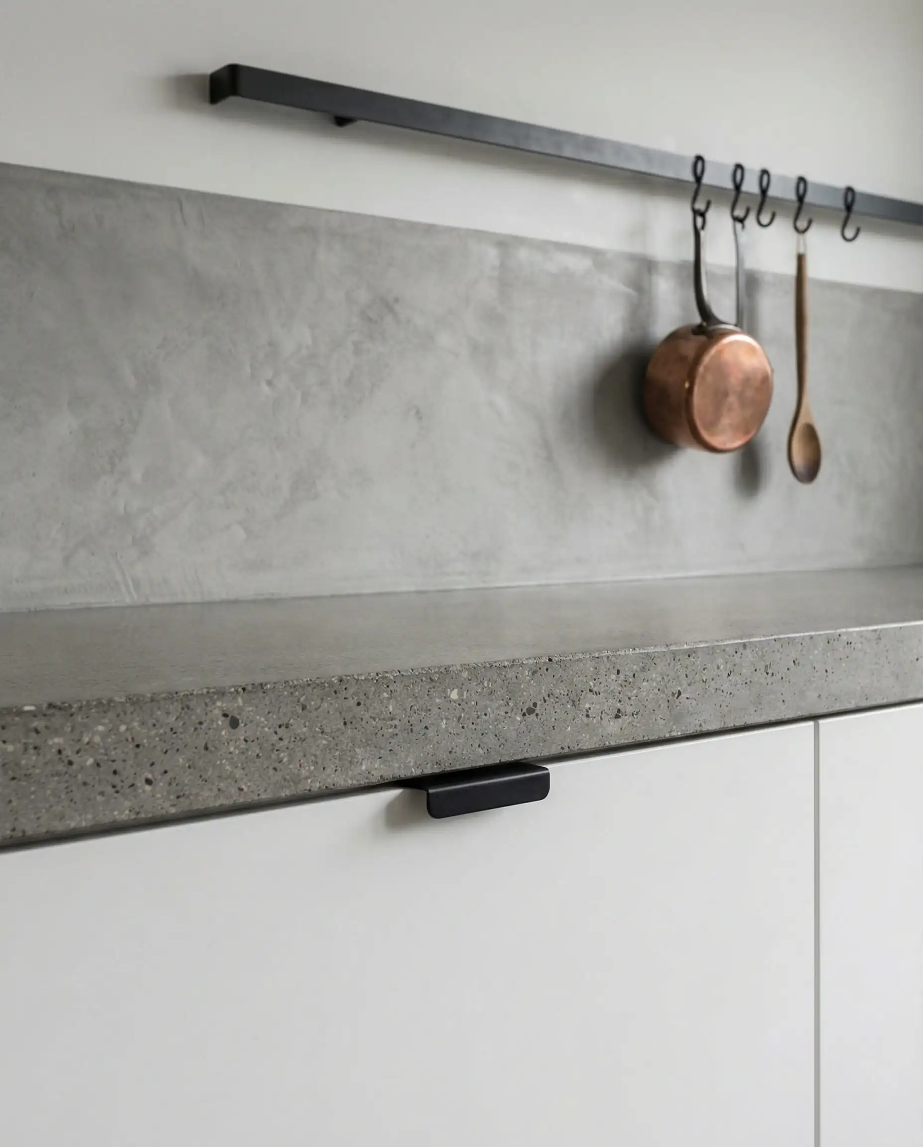 Layered composition of white base cabinets with black pulls meeting a raw grey concrete countertop.
