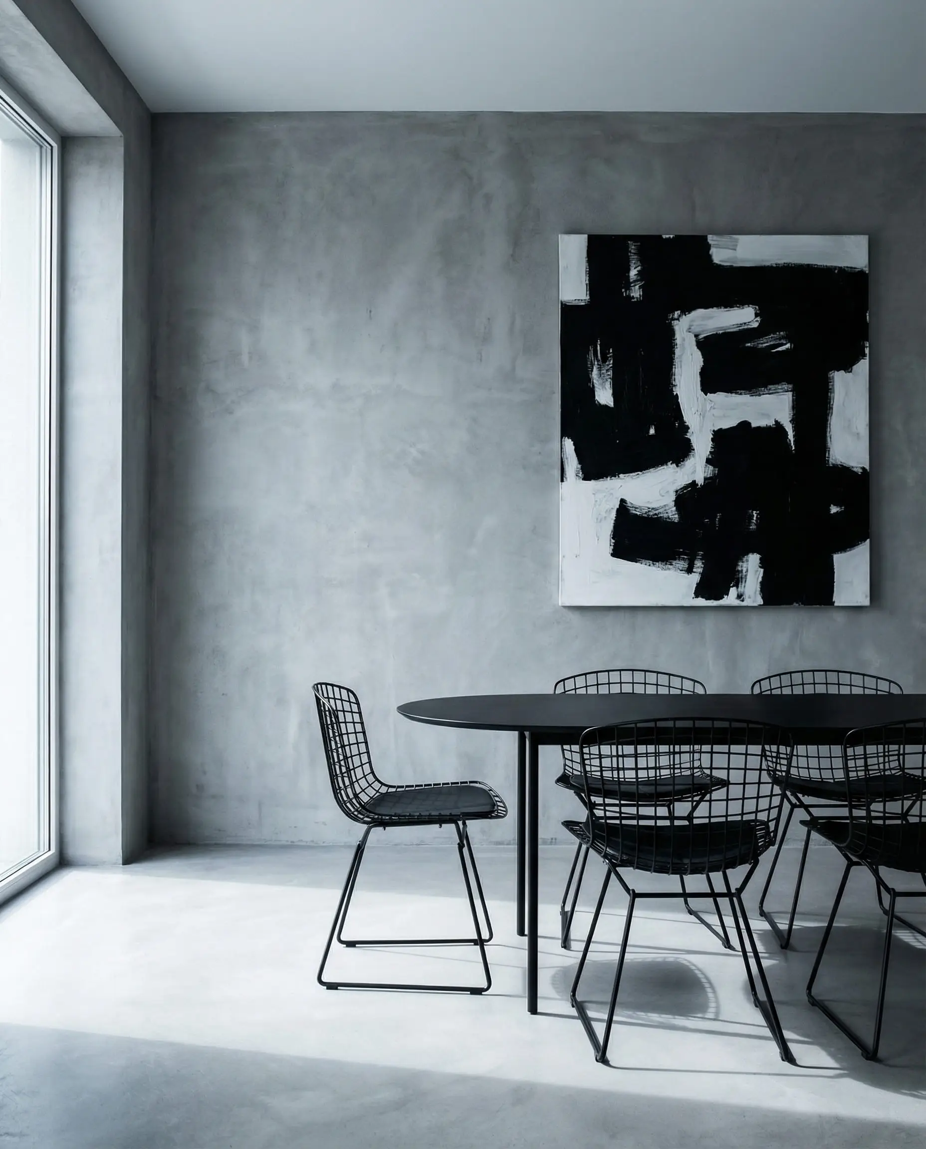 Brutalist chic dining room with a seamless concrete grey microcement accent wall and black wire-frame dining chairs.