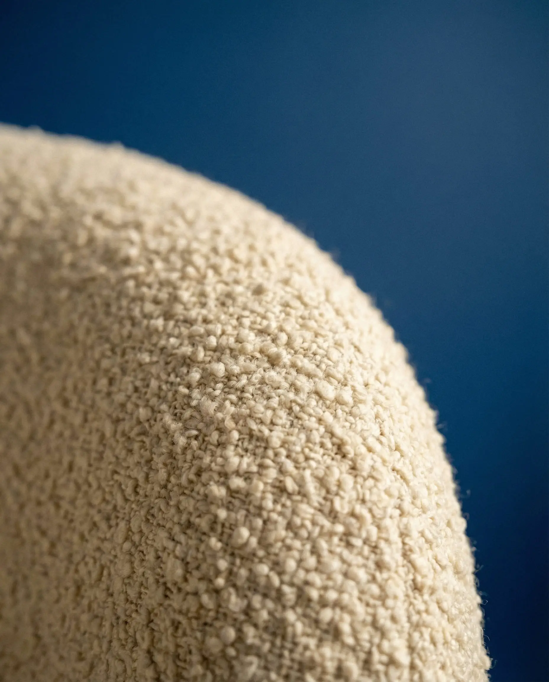 Macro shot of cream bouclé fabric texture against a royal blue wall.