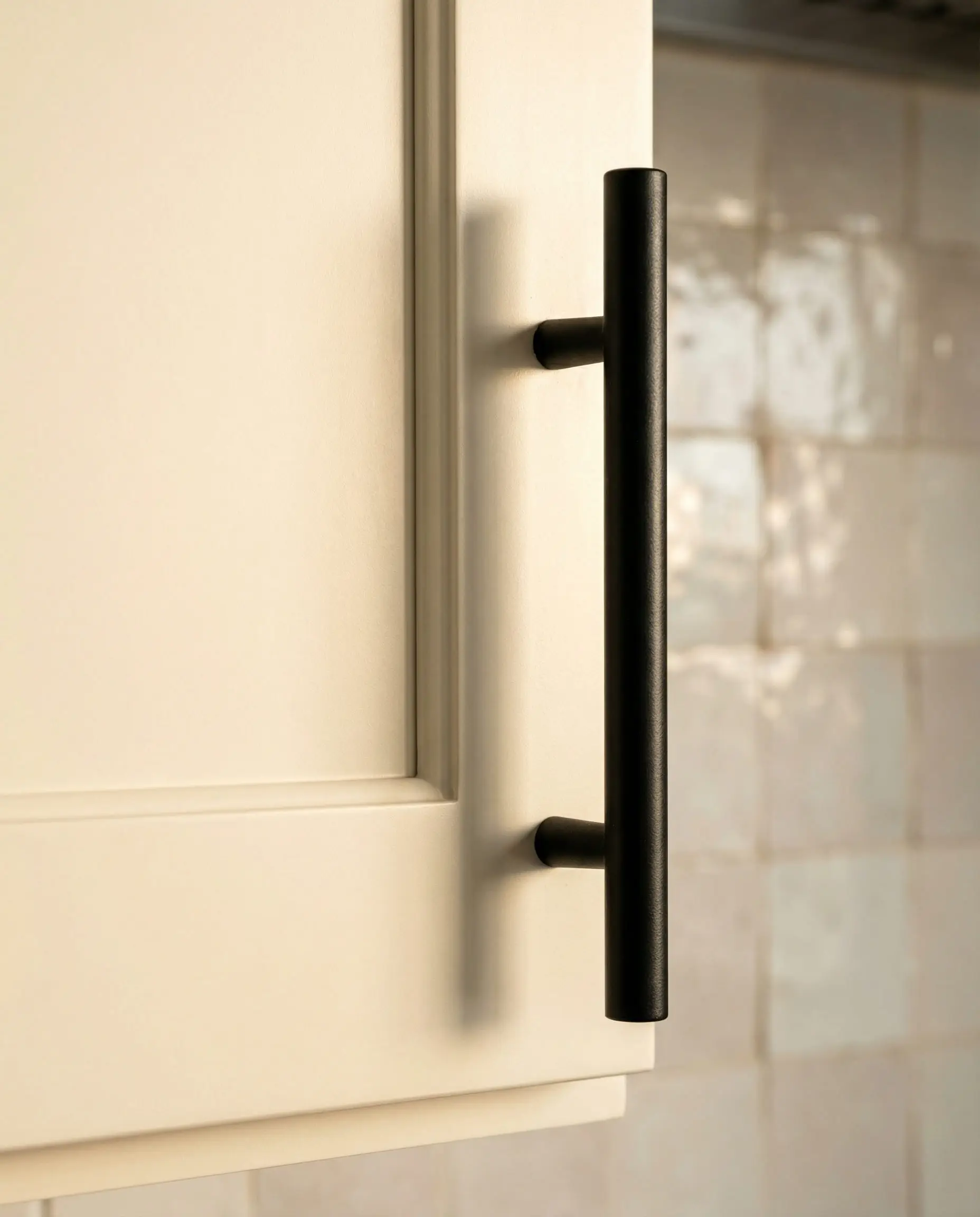 Close-up detail of creamy Swiss Coffee painted cabinets featuring sleek matte black T-bar pulls, highlighting the warm undertone trend.