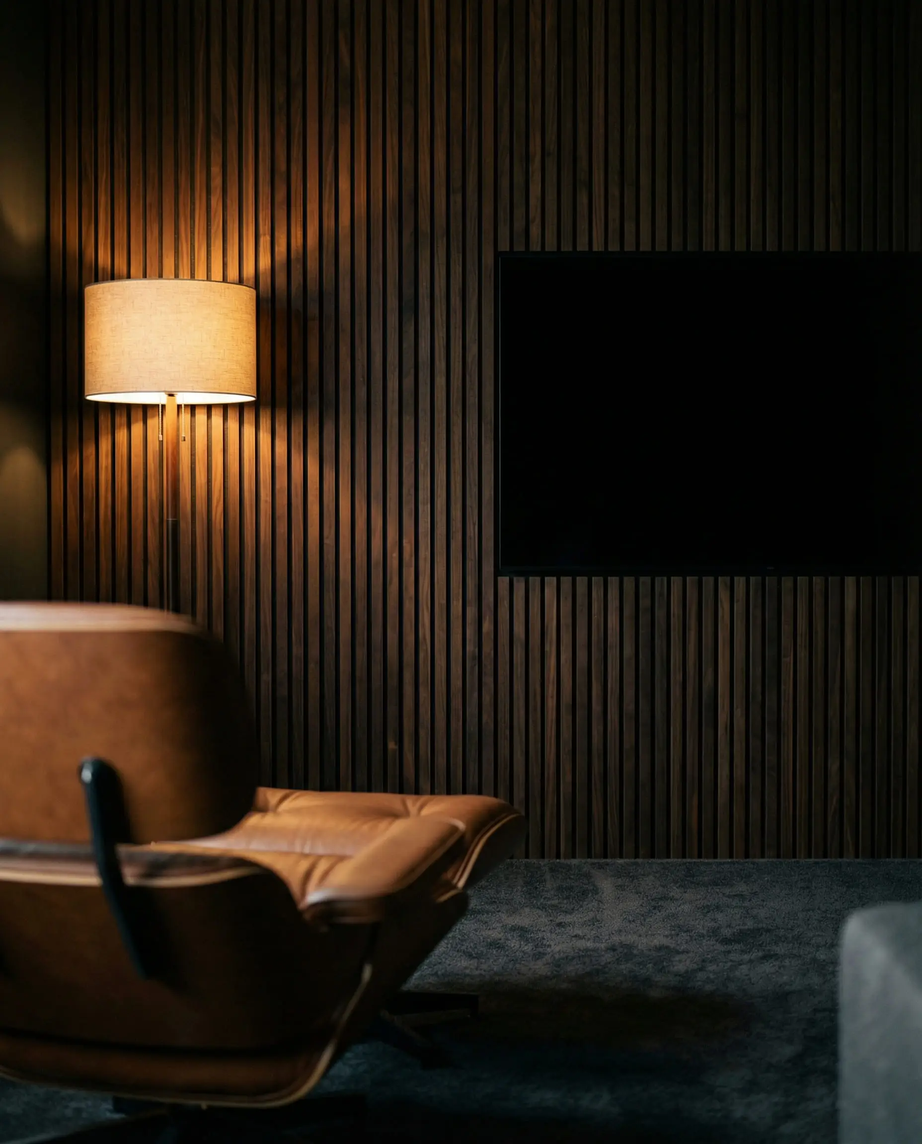 Moody living room with a dark walnut acoustic panel feature wall that camouflages the black TV screen.