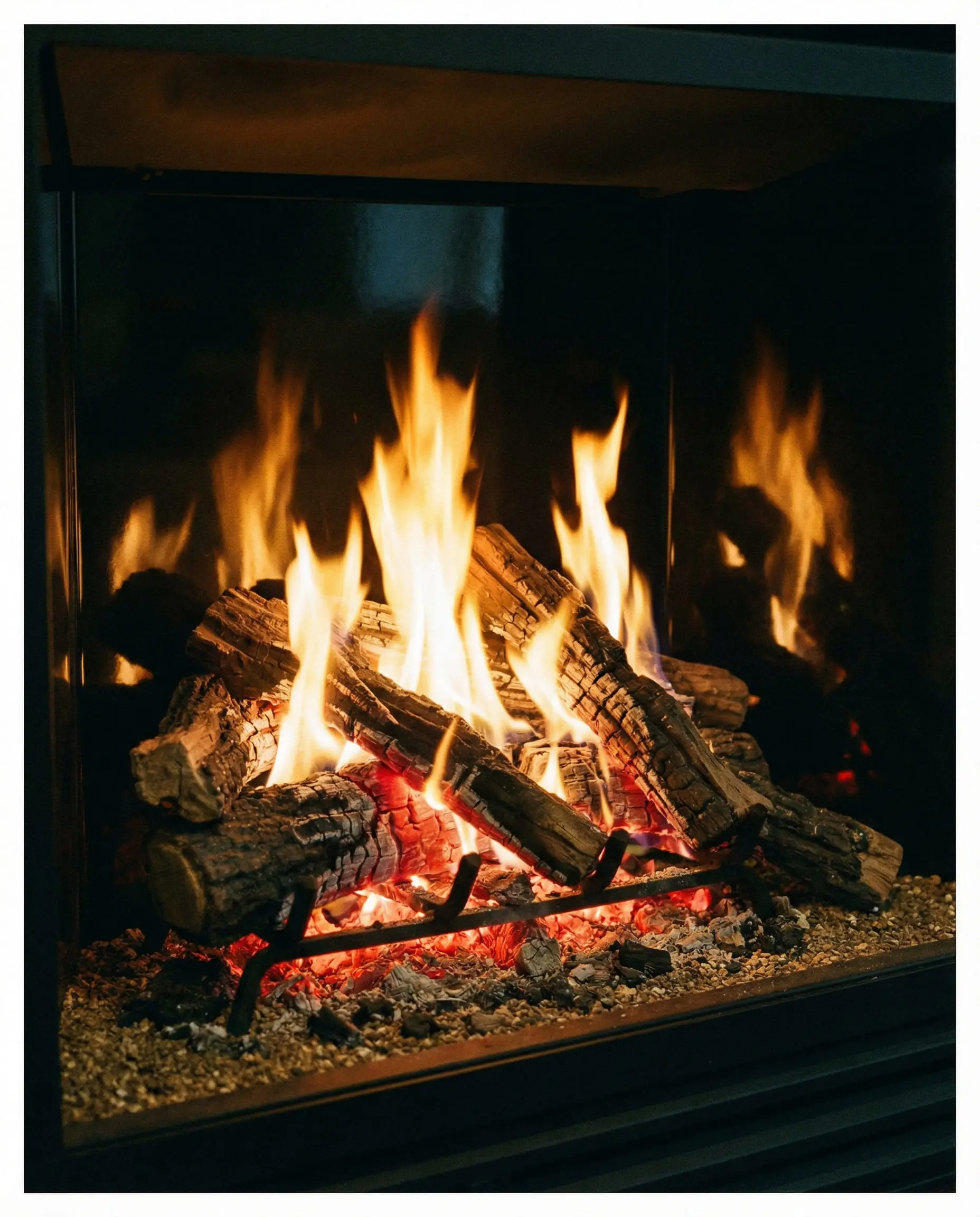 Close-up of realistic ceramic driftwood logs and glowing embers inside a direct-vent gas fireplace.