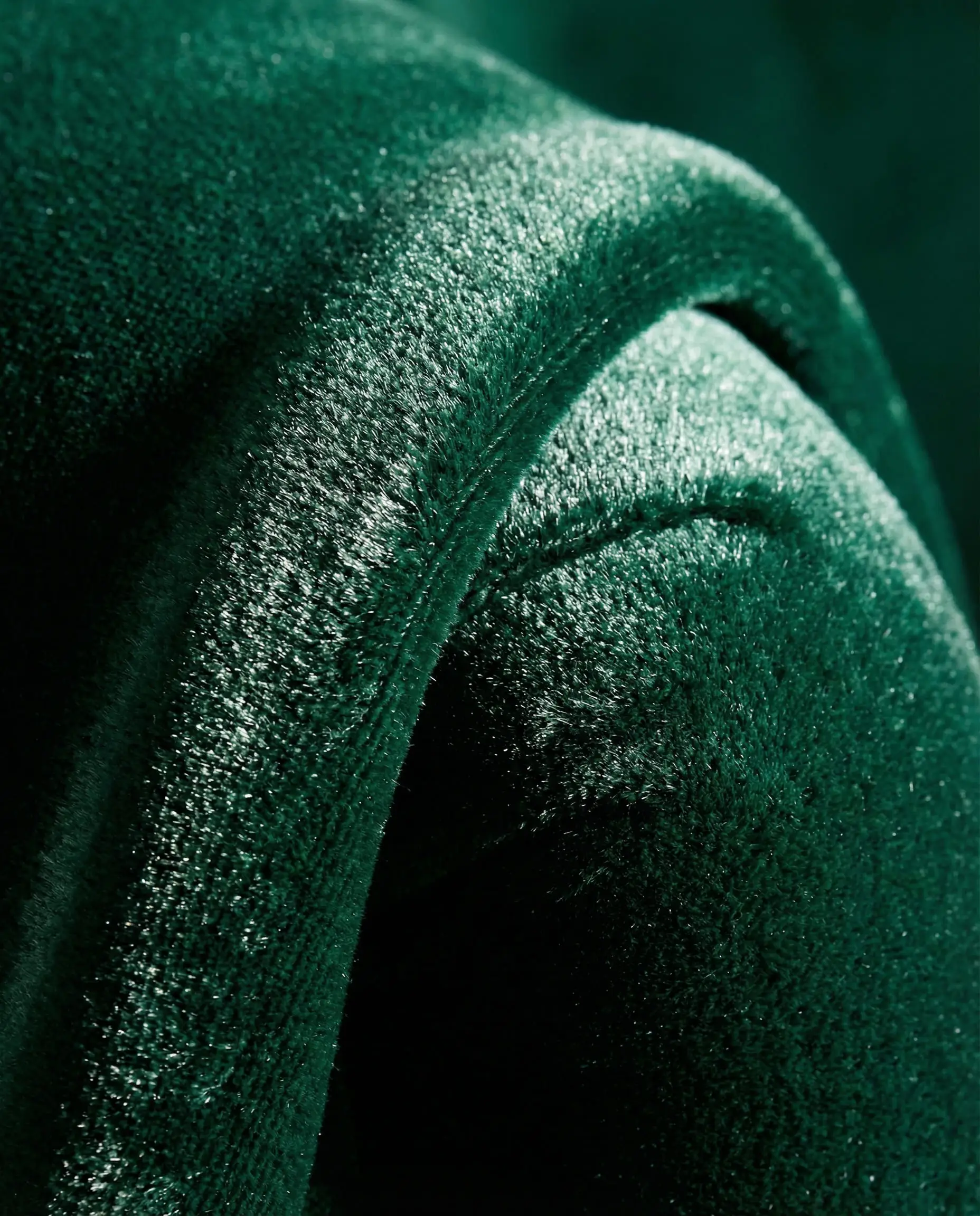 Macro photography of draped emerald green velvet fabric showing the plush texture and light reflection.