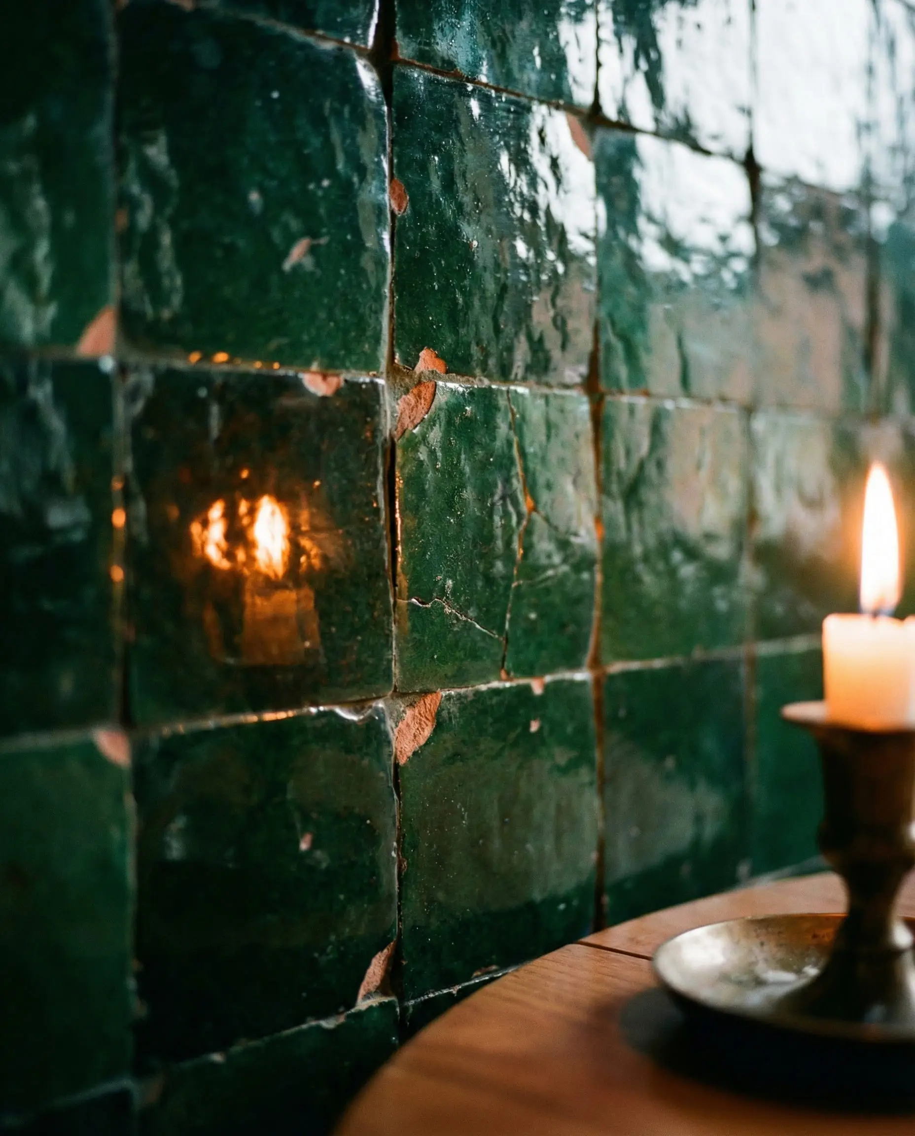 Close-up of emerald green Zellige tiles with uneven glazed surfaces reflecting warm candlelight.