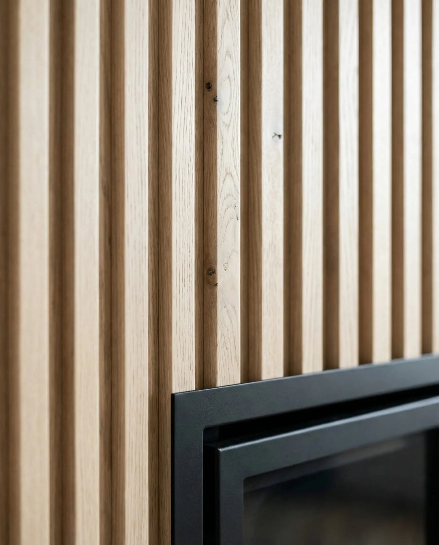 Close-up detail of vertical fluted white oak wood paneling on a modern fireplace wall, highlighting the texture and grain.