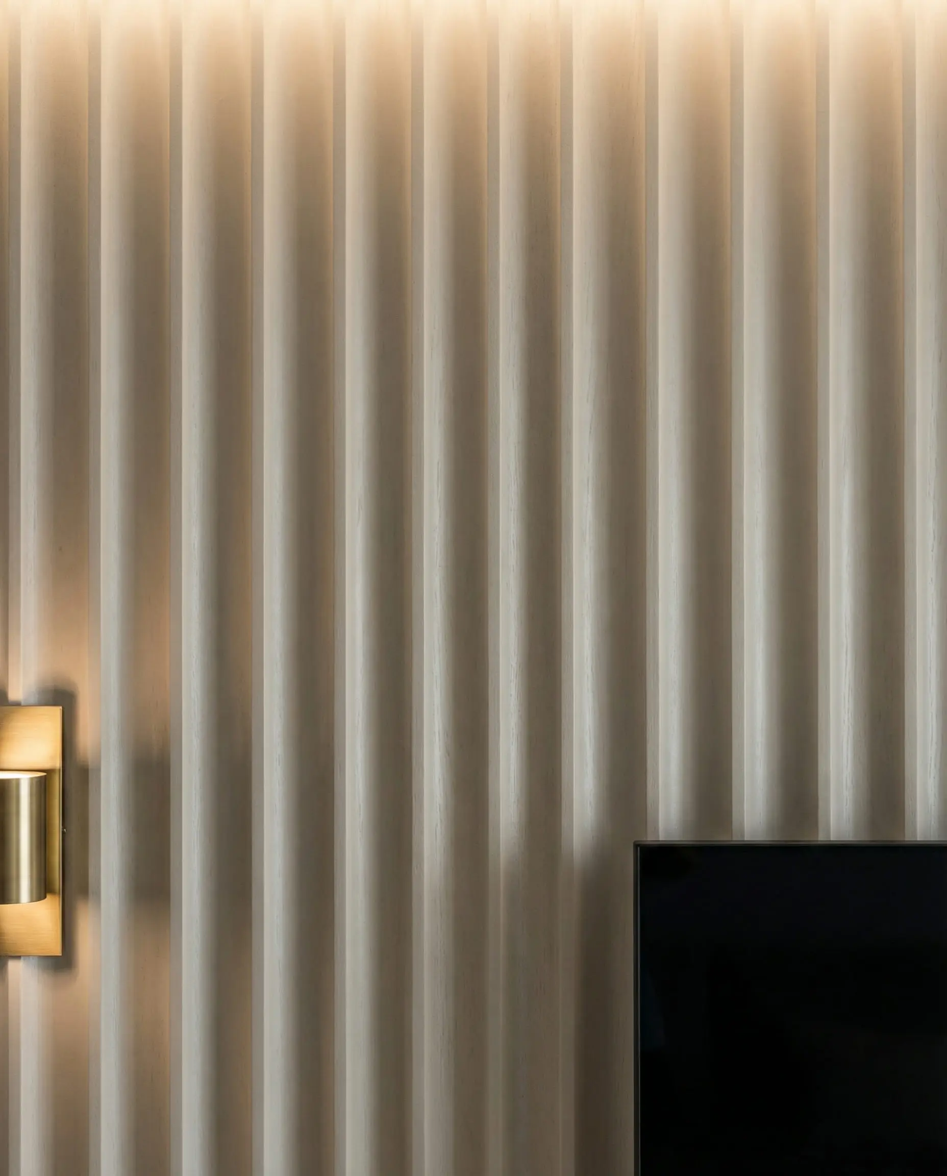 Close-up of a fluted wood wall panel painted in greige with a curved texture behind a modern television.