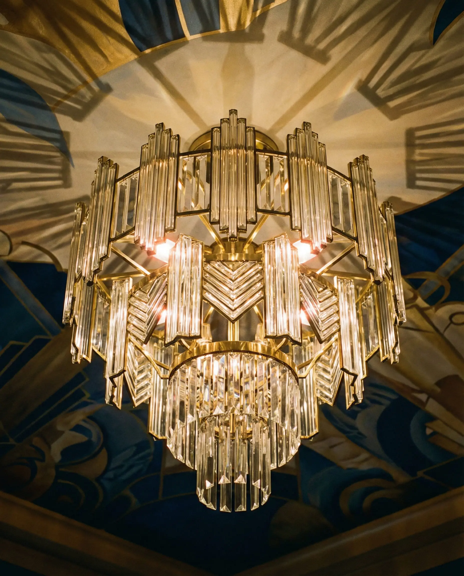 Low angle view of a brass and glass geometric chandelier casting angular shadows on the ceiling.