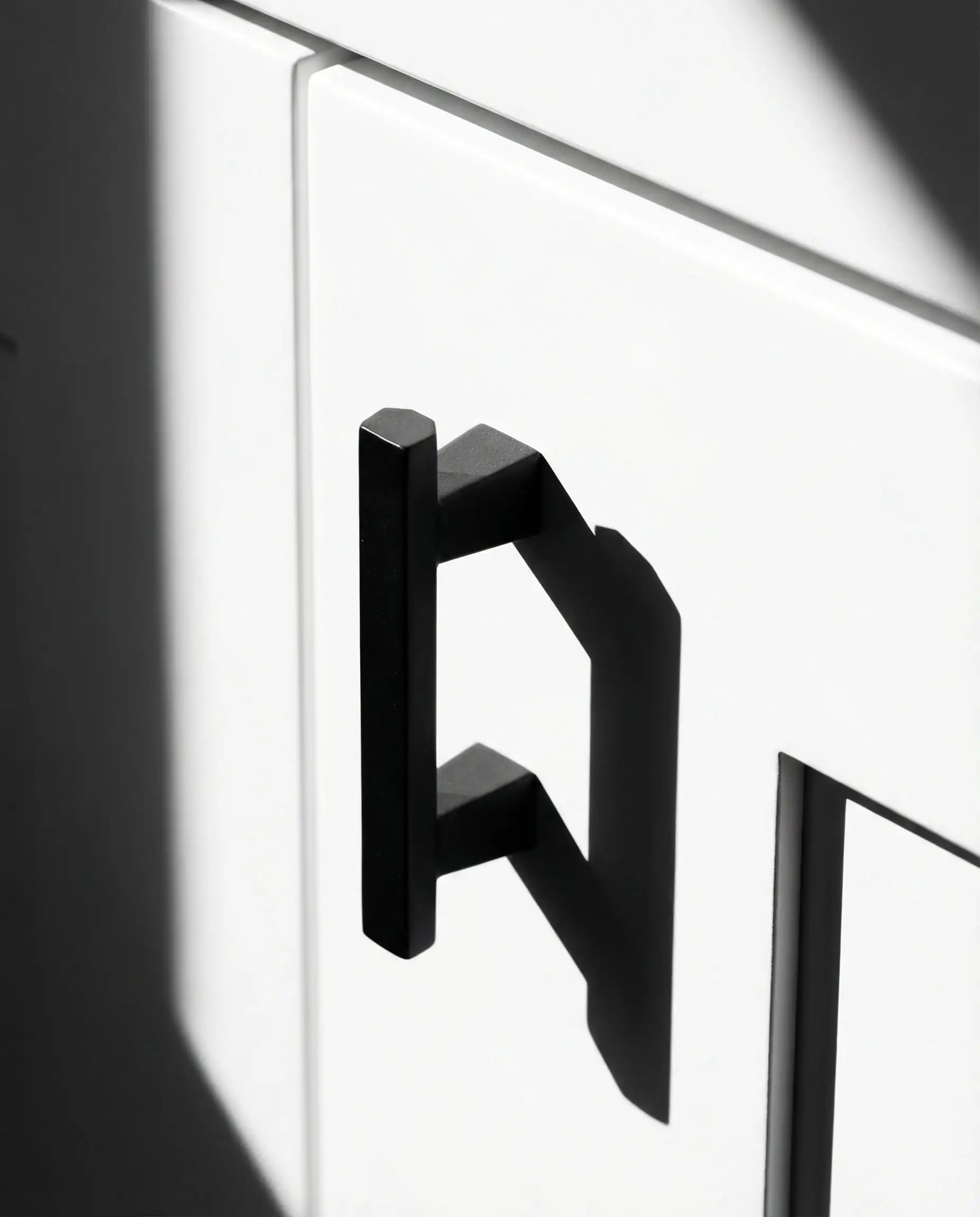 Detail of a hexagonal matte black cabinet knob casting sharp shadows on a pristine white surface.