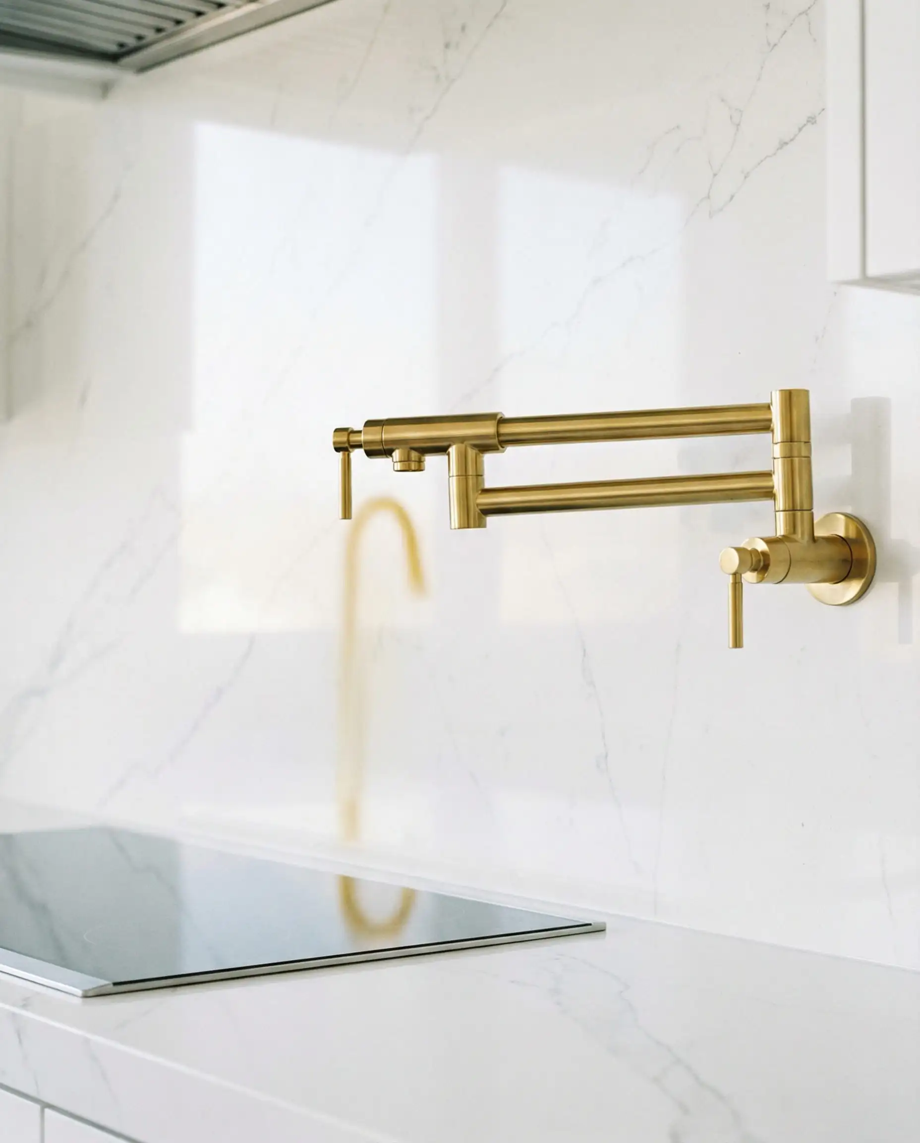 Gold articulated pot filler faucet mounted on a seamless white quartz backsplash.
