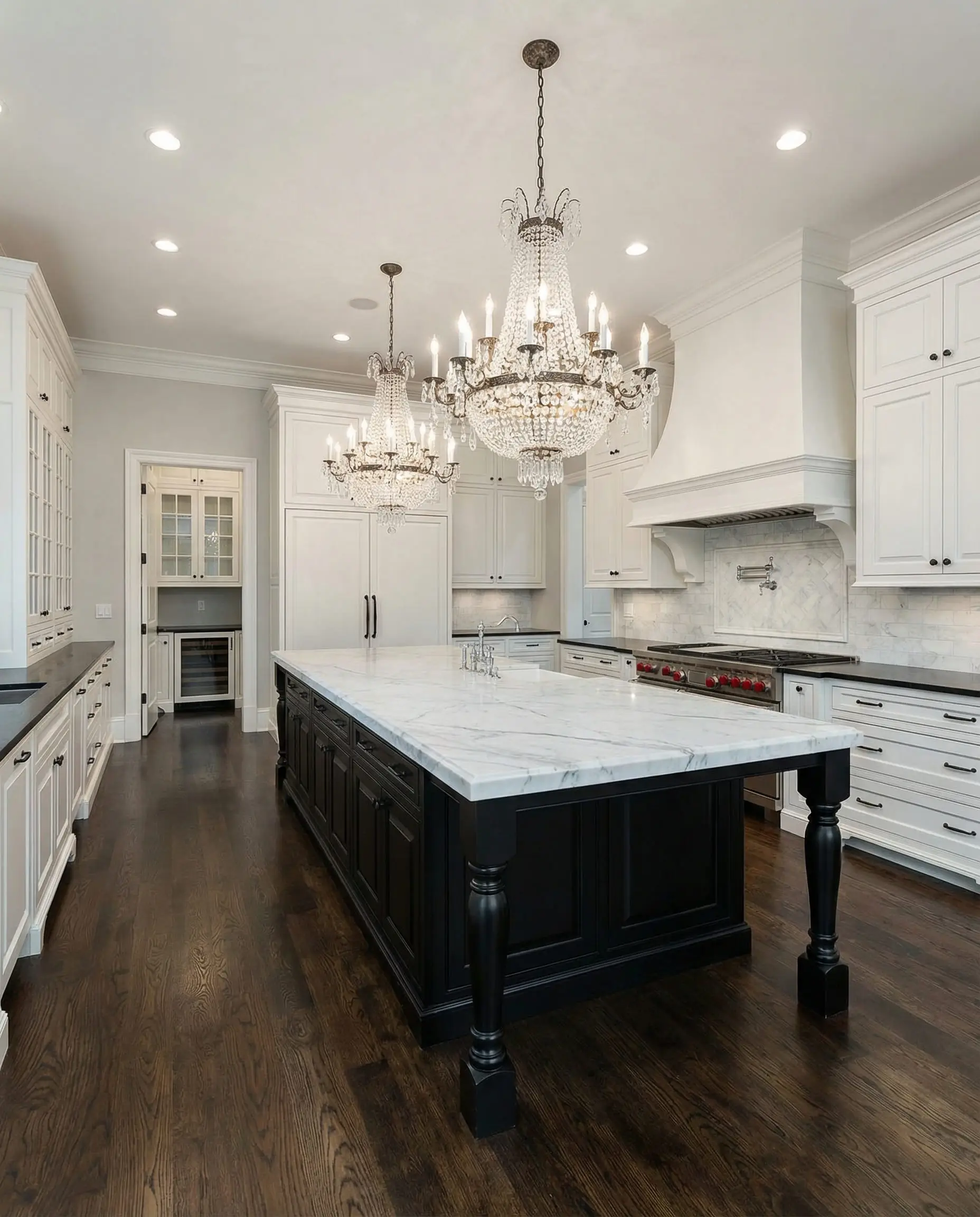 Wide shot of a grand traditional kitchen with a large island, crystal chandeliers, and white cabinets with black hardware.